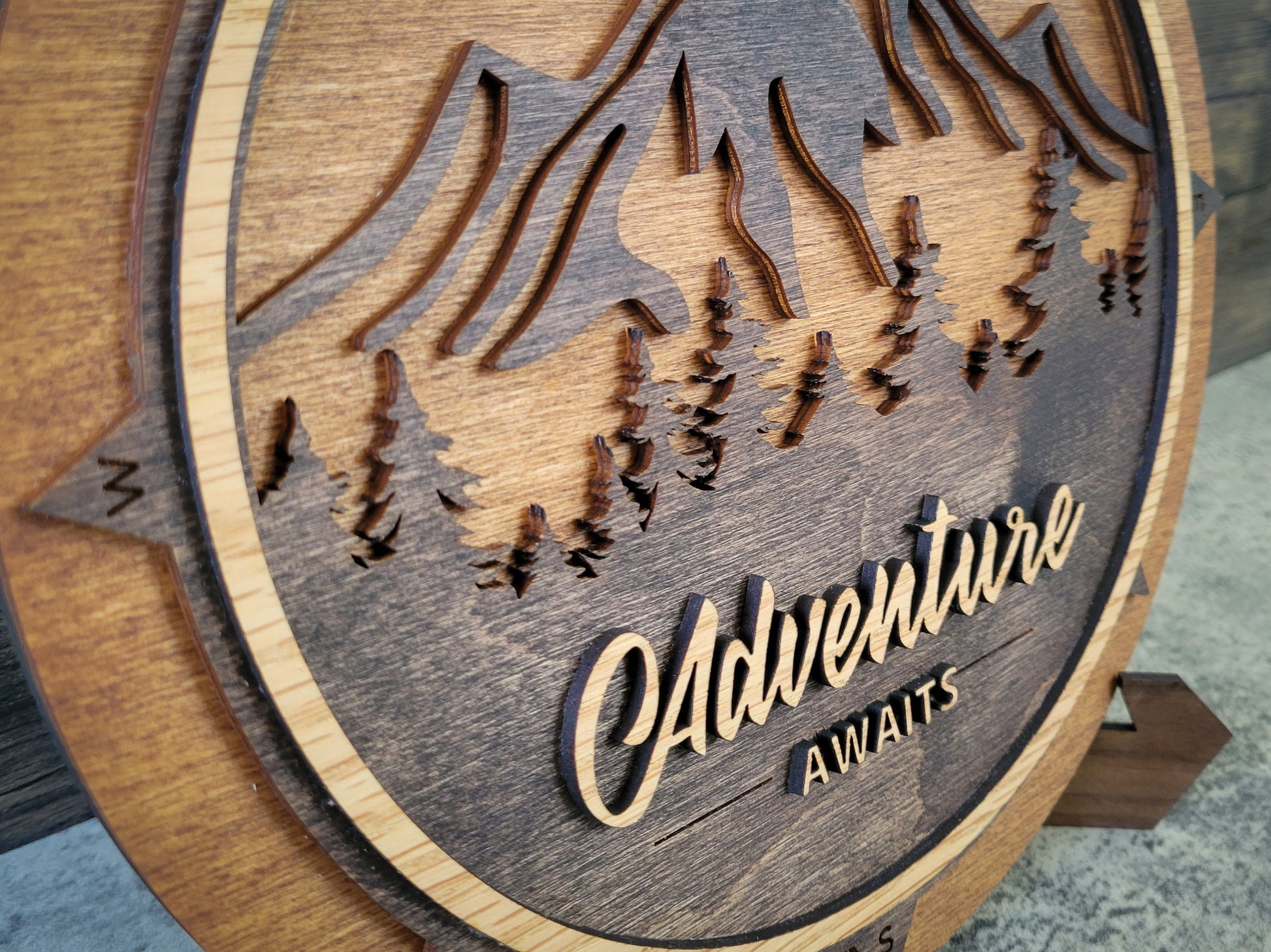 Wooden plaque with laser-cut design of trees and the text 'Adventure Awaits'.