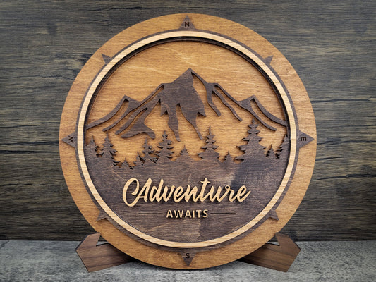 Wooden plaque with mountain design and 'Adventure Awaits' text on a wooden background