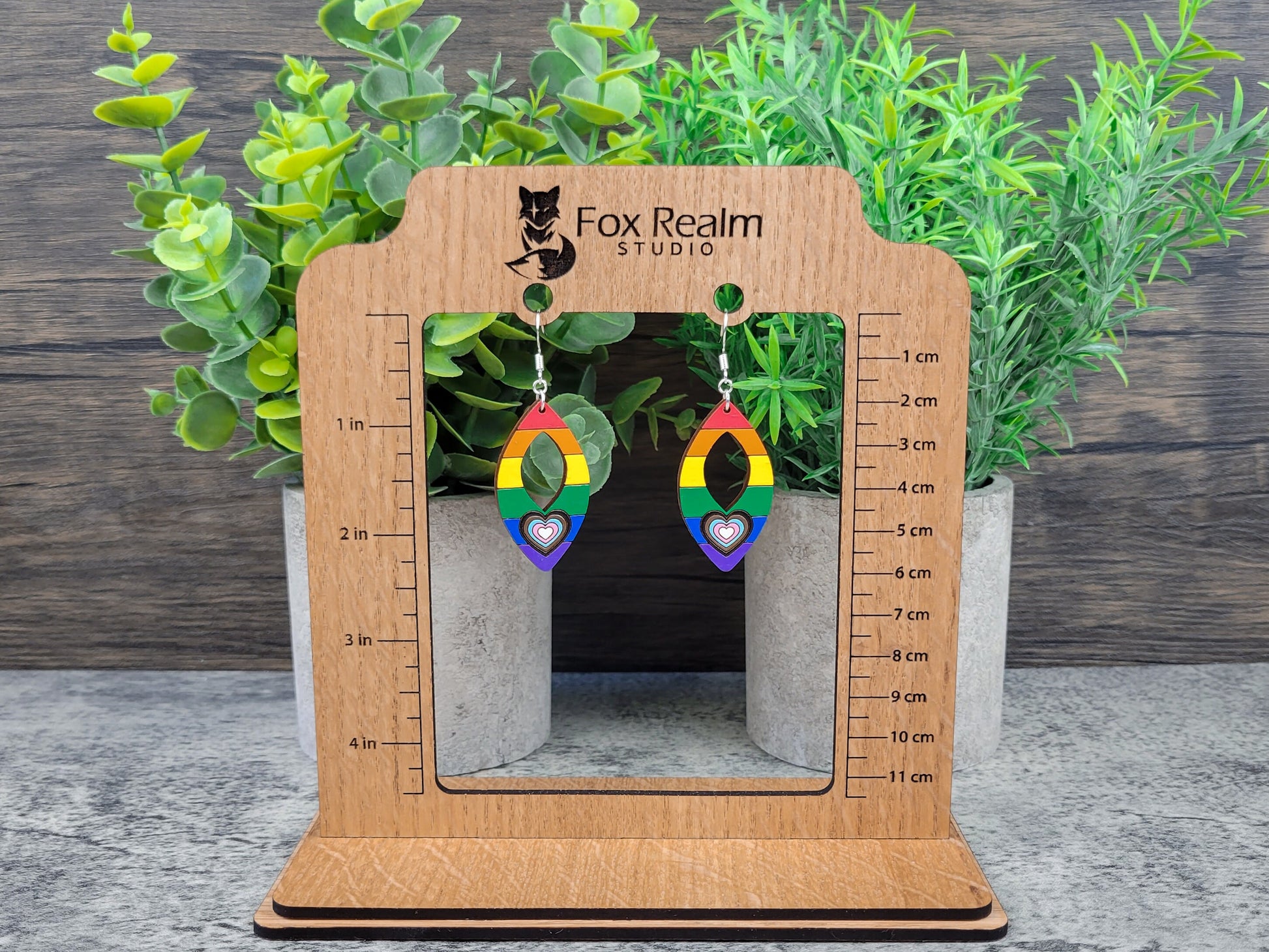 Rainbow heart earrings on a wooden stand for scale with plants in the background