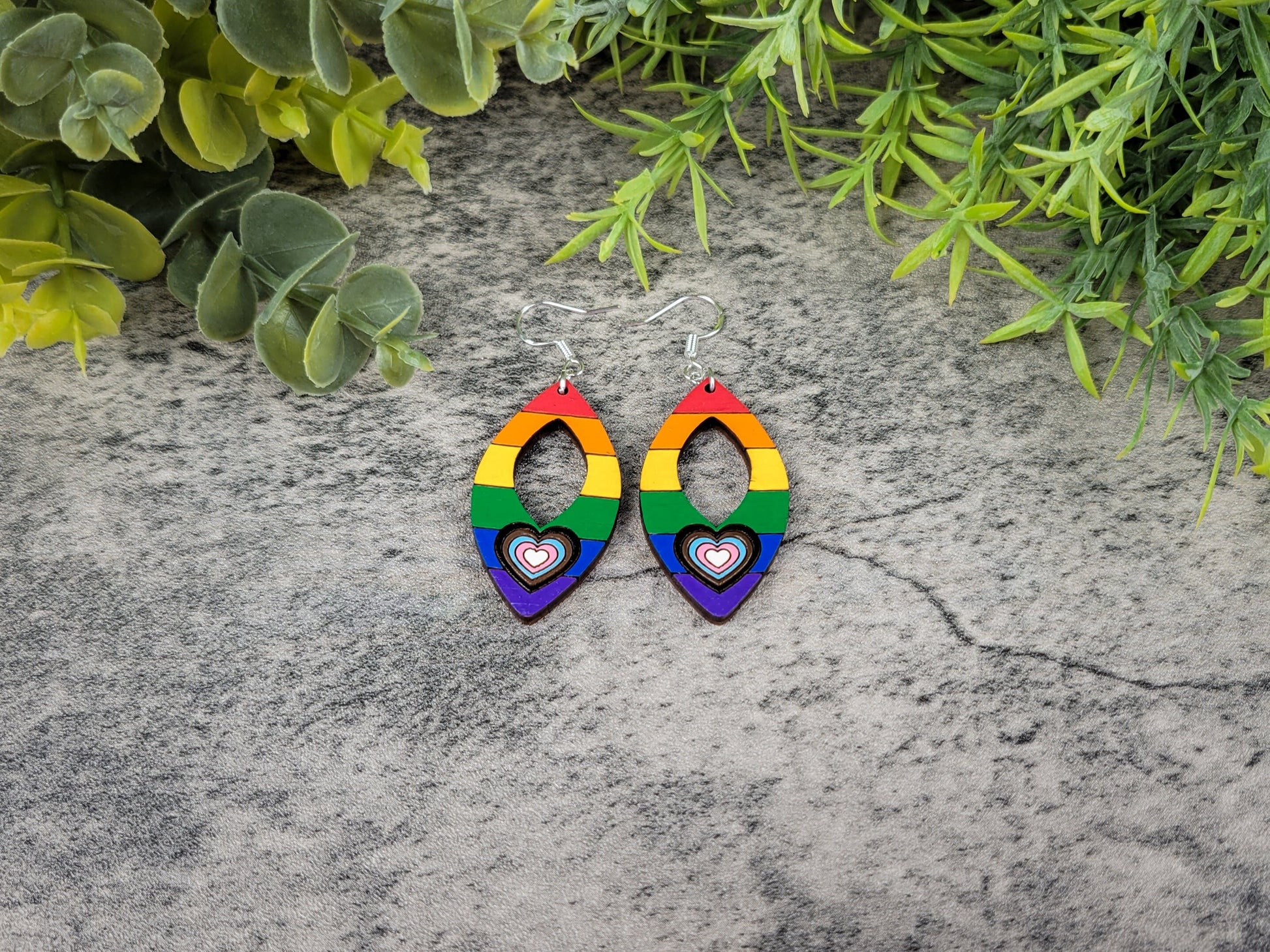 Rainbow heart earrings on a stone surface with greenery