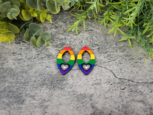Rainbow heart earrings on a stone surface with greenery