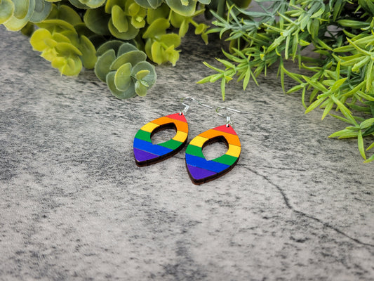 Rainbow heart-shaped earrings on a textured surface with green foliage in the background, angled view