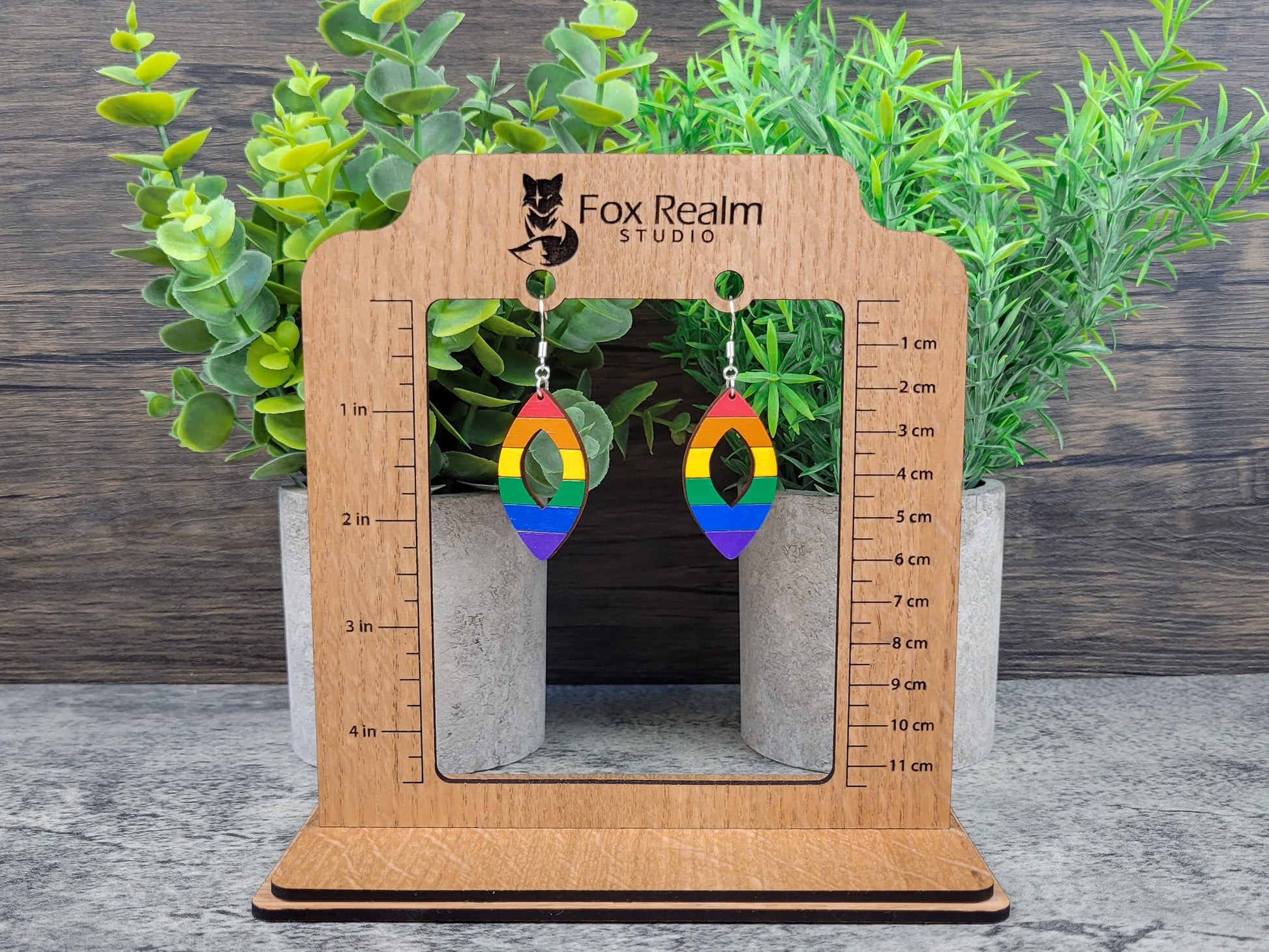 Rainbow earrings on a wooden scale stand with plants in the background