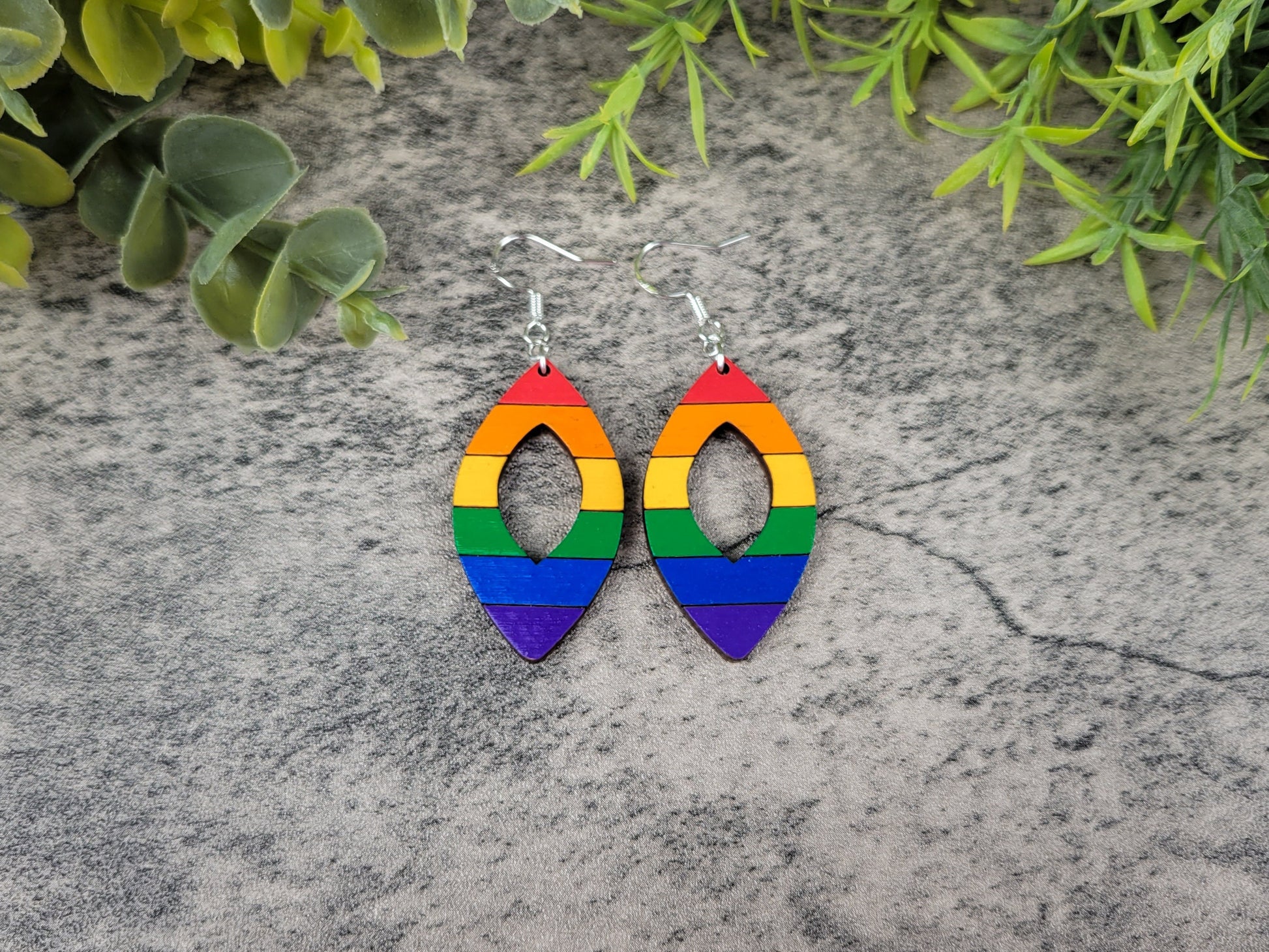Rainbow-colored earrings on a textured stone surface with green leaves in the background
