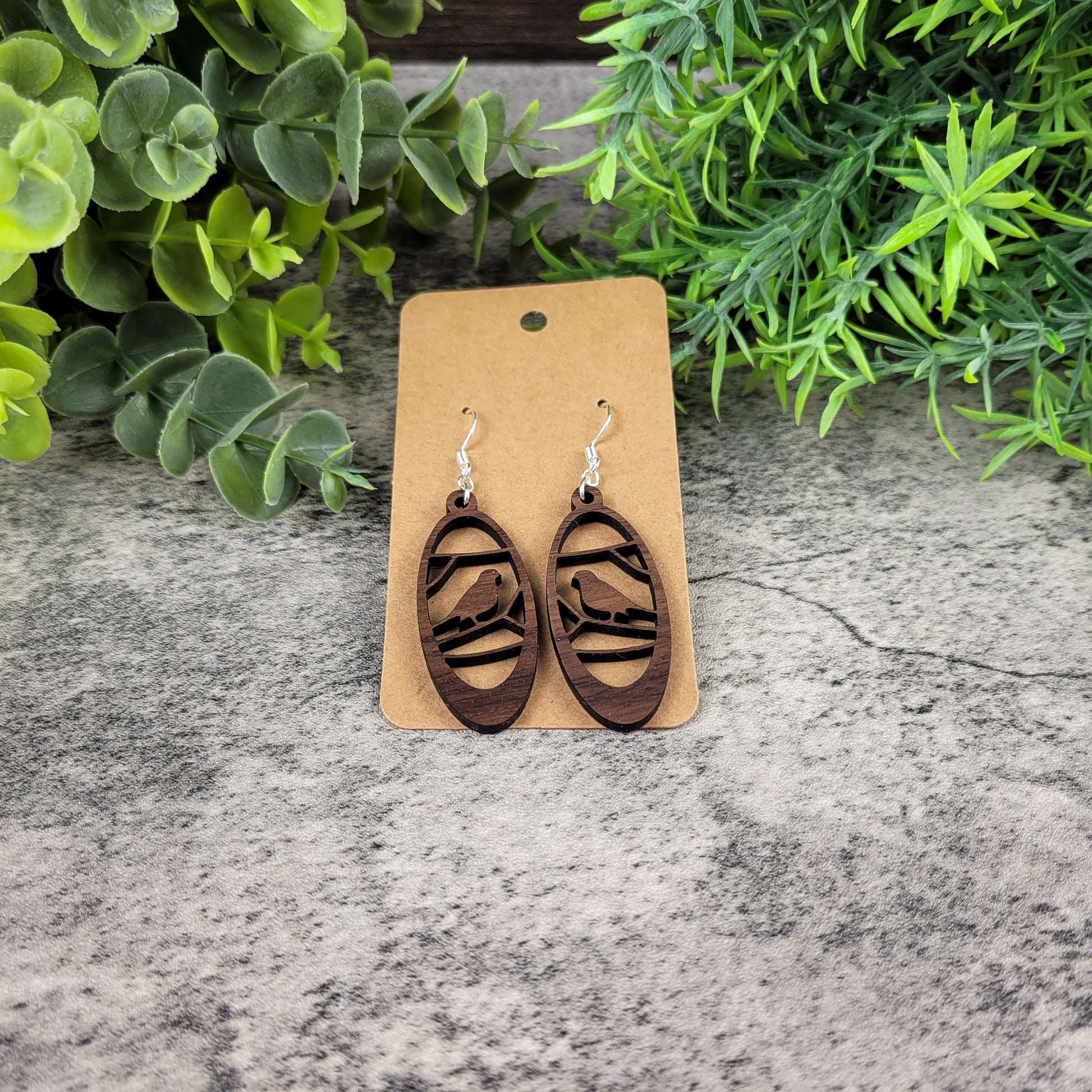 Lightweight walnut wood earrings featuring a bird in branches design on hypoallergenic sterling silver-plated ear wires - angled front view