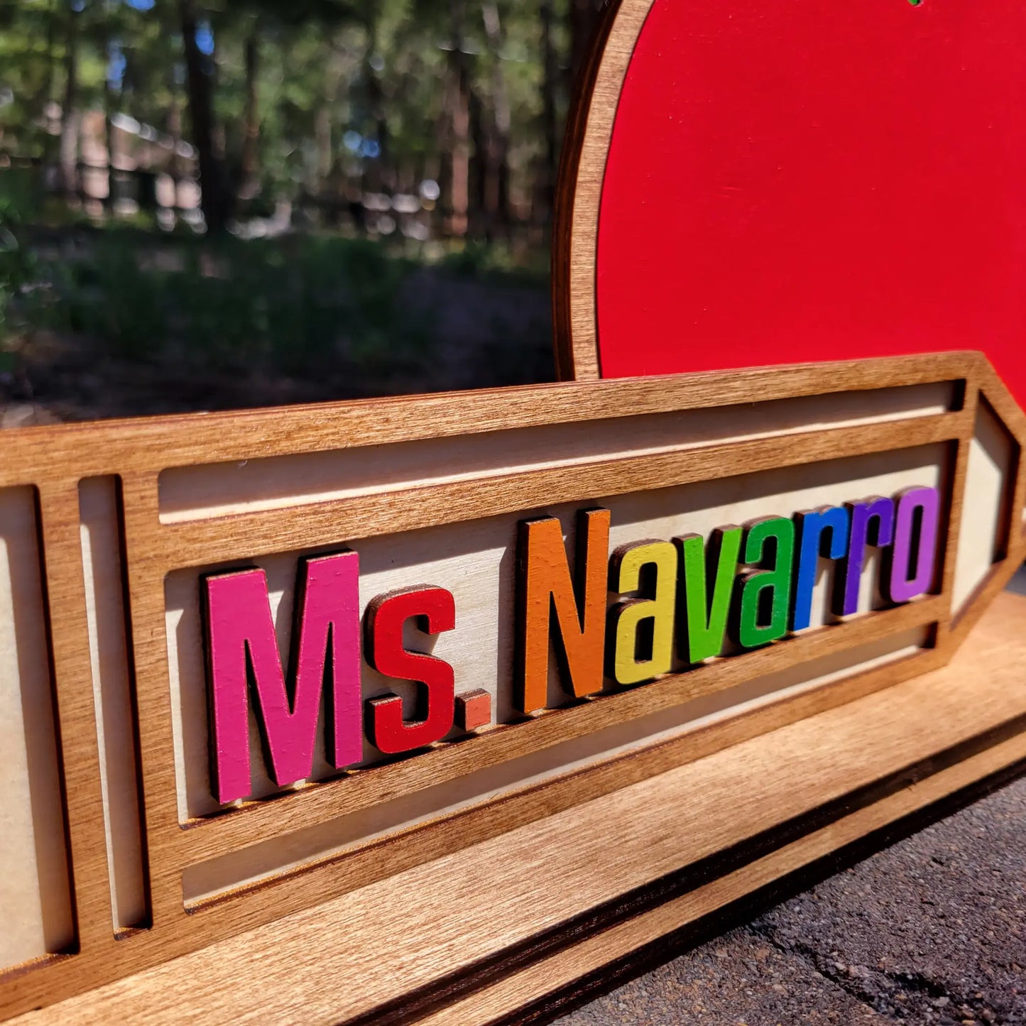 Colorful nameplate with 'Ms. Navarro' on a wooden frame outdoors.
