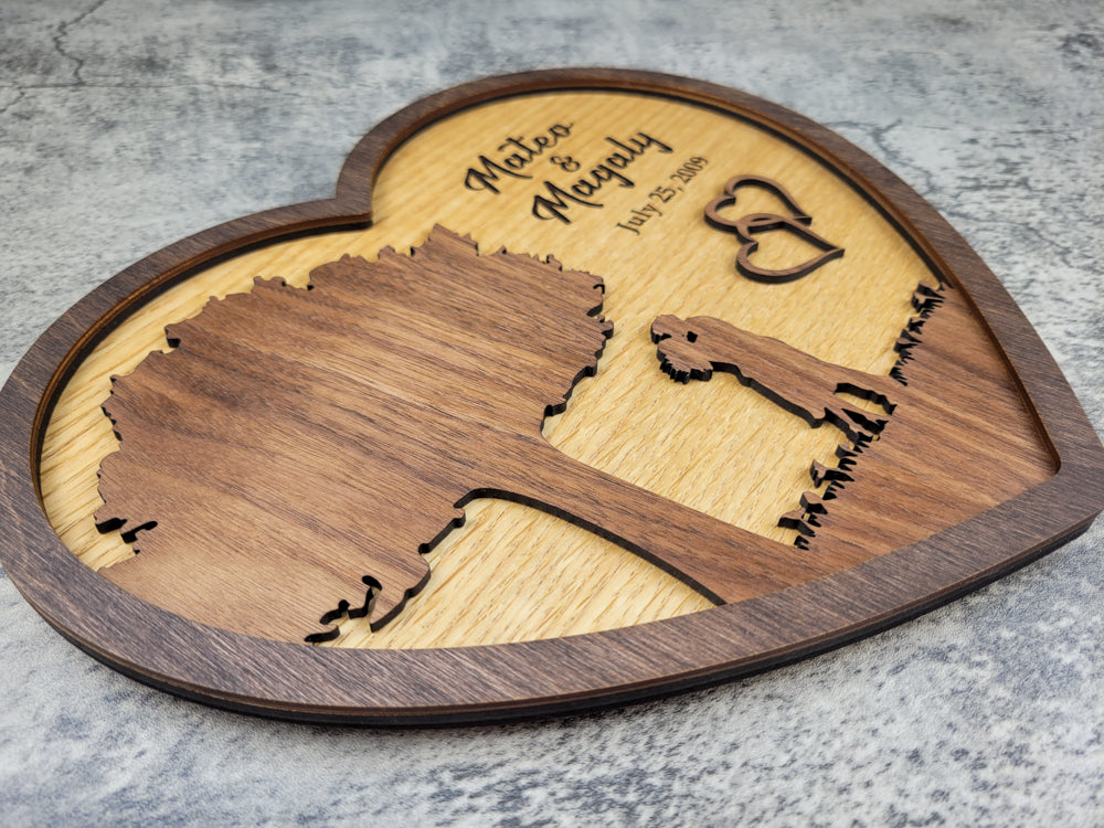 Wooden heart-shaped plaque with engraved map and couple's names on a gray surface