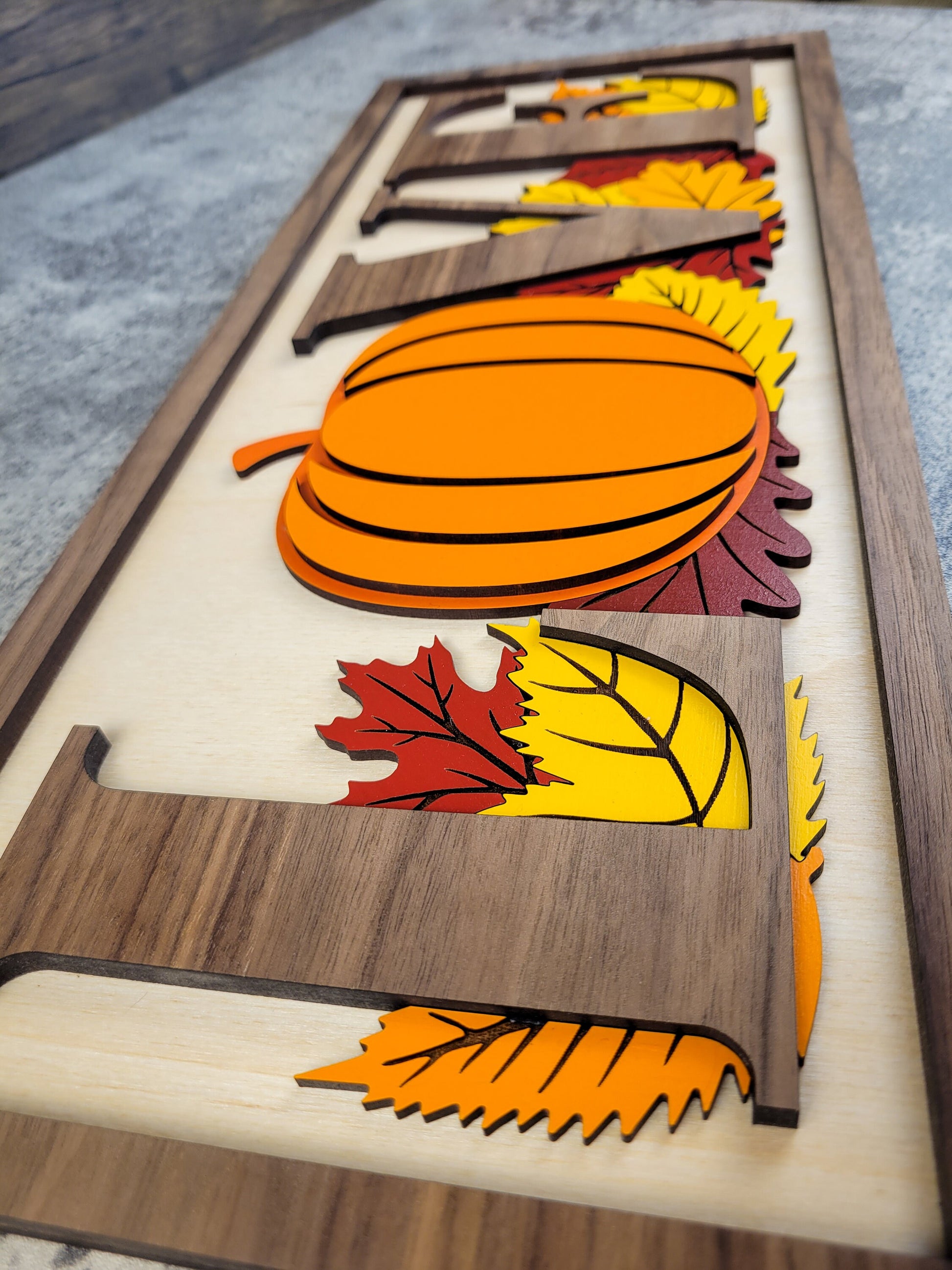Wooden decorative panel with cut-out shapes of a pumpkin, leaves, and sunflower on a wooden surface.