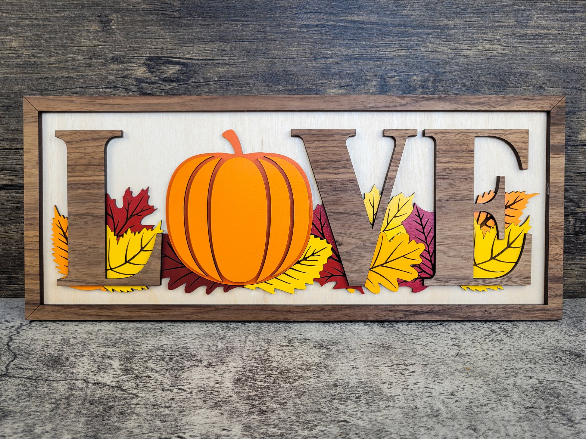 Decorative sign with 'LOVE' letters and pumpkin, against a wooden background
