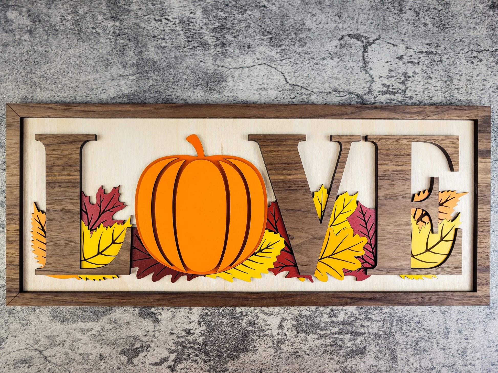 Decorative sign with 'LOVE' letters, pumpkin, and leaves on a textured gray background