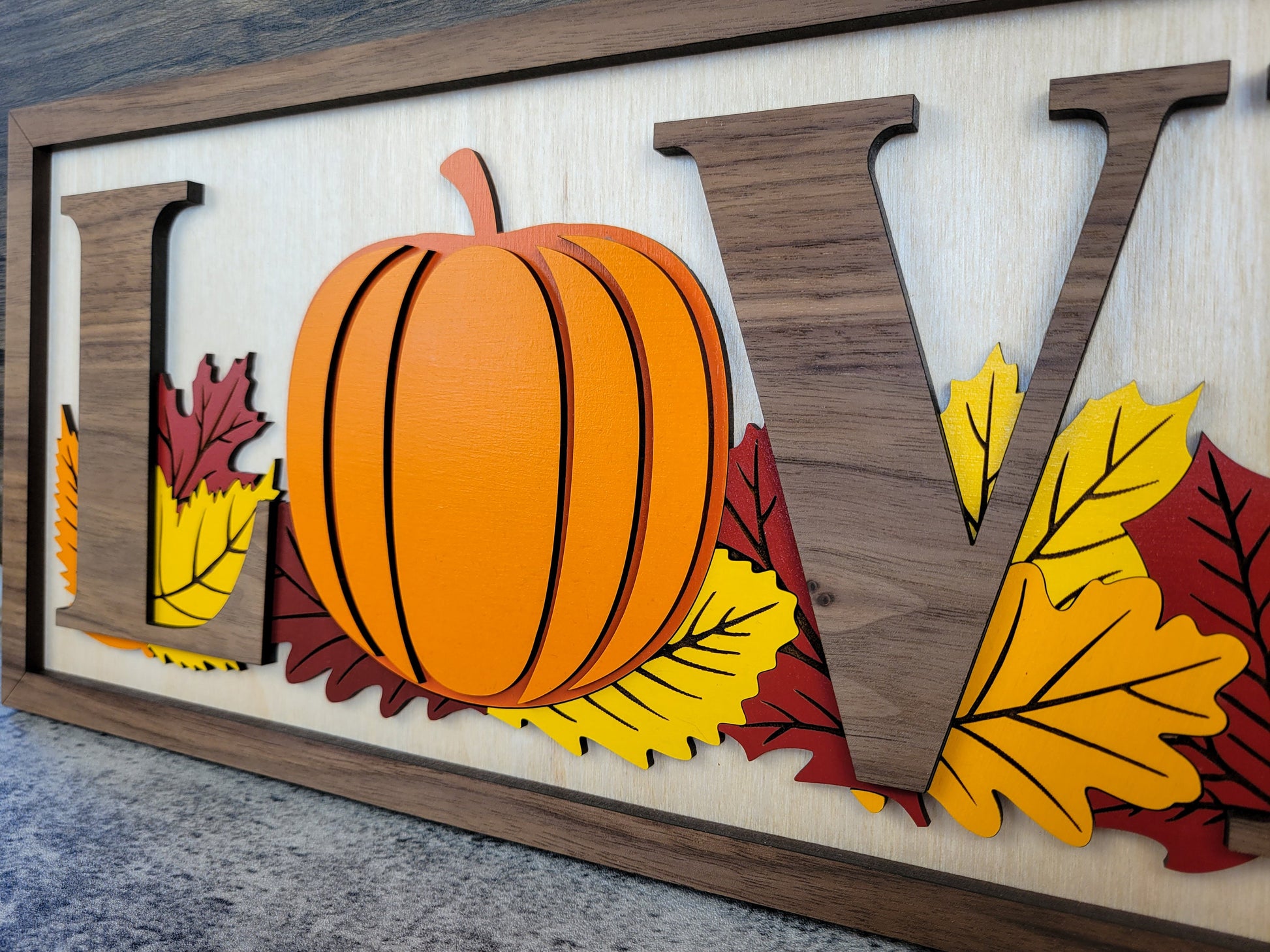 Decorative sign with 'LOV' letters and a pumpkin surrounded by leaves on a wooden background.
