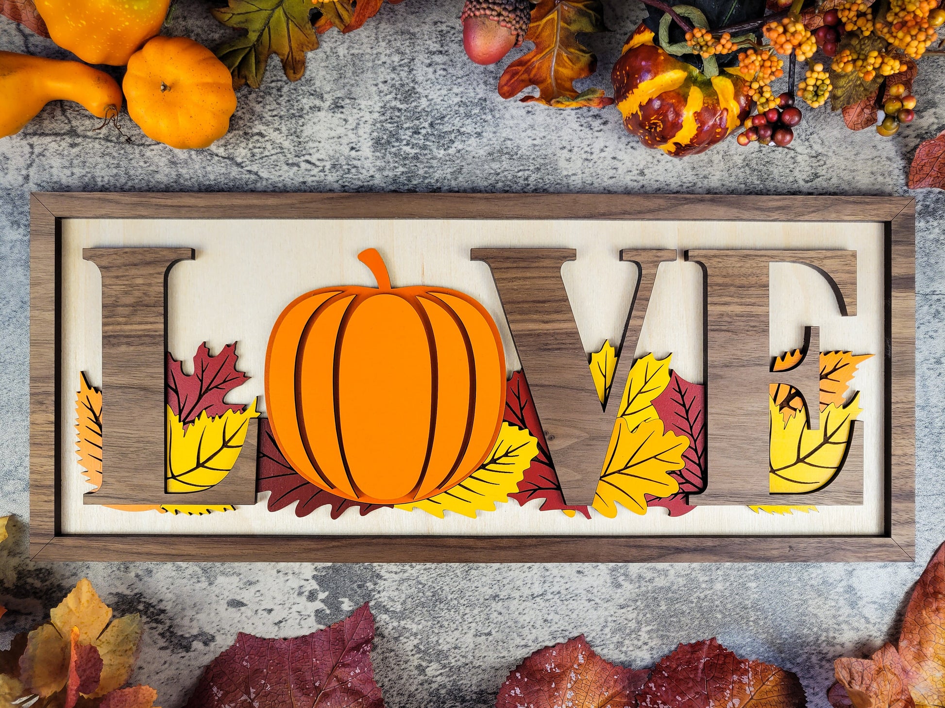 Decorative sign with 'LOVE' and pumpkin design on a rustic background with autumn leaves and gourds.