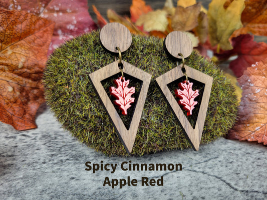 Wooden earrings with red leaf design on a moss ball with autumn leaves in the background