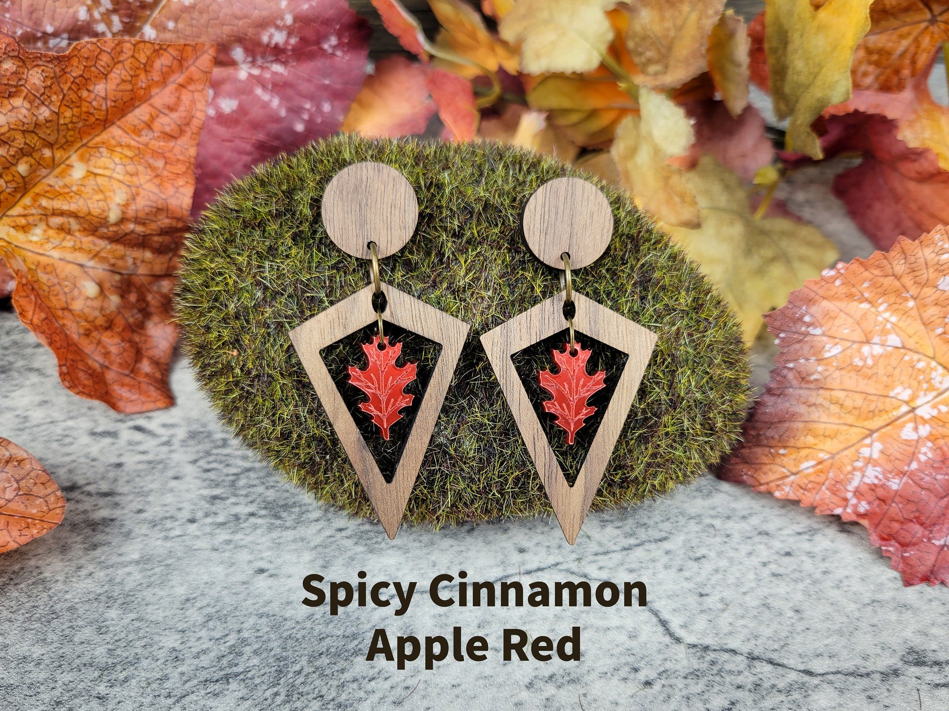 Wooden earrings with red leaf design on a moss and leaf background, labeled 'Spicy Cinnamon Apple Red'.