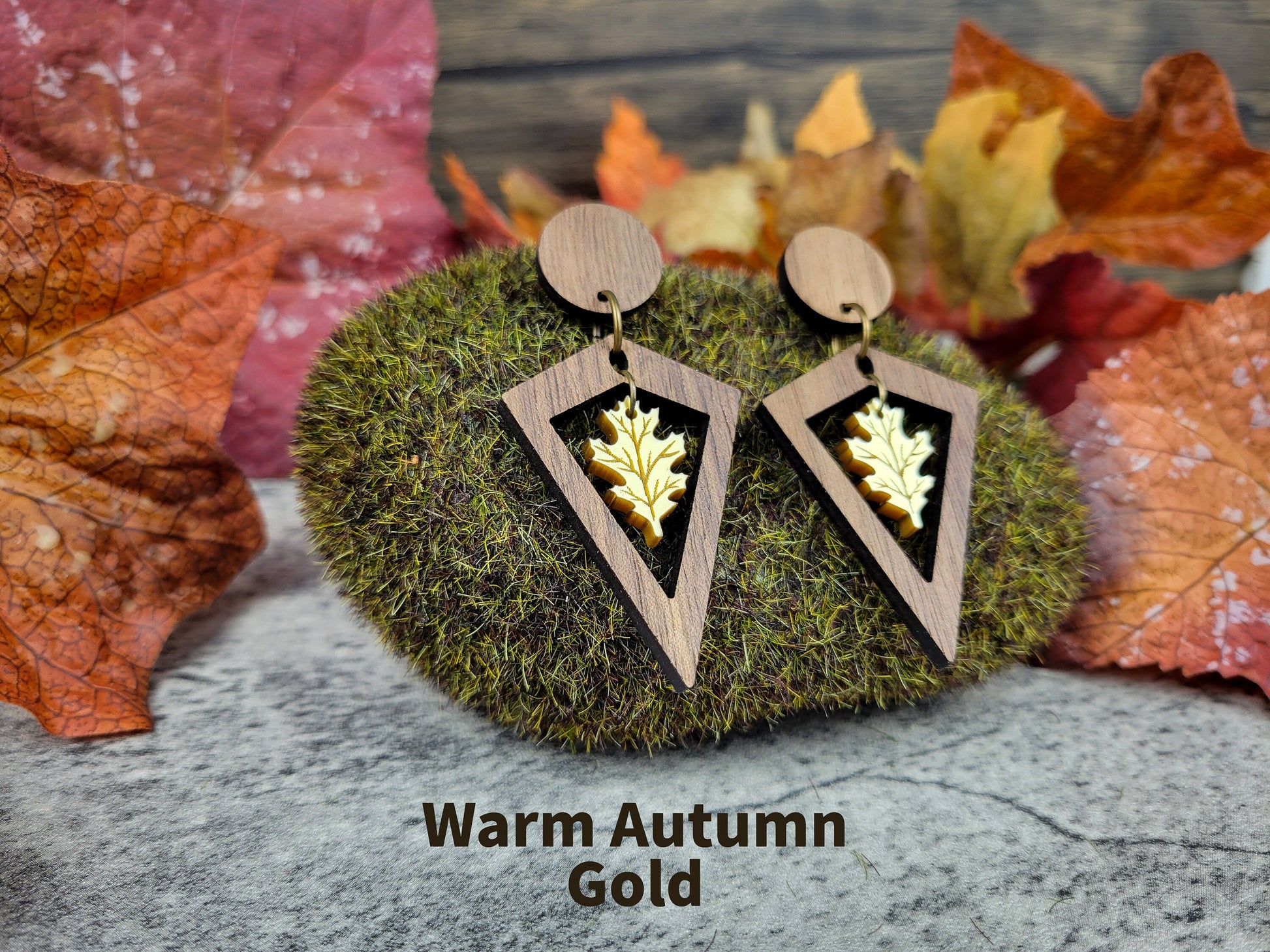 Wooden earrings with leaf design on a moss ball with autumn leaves in the background