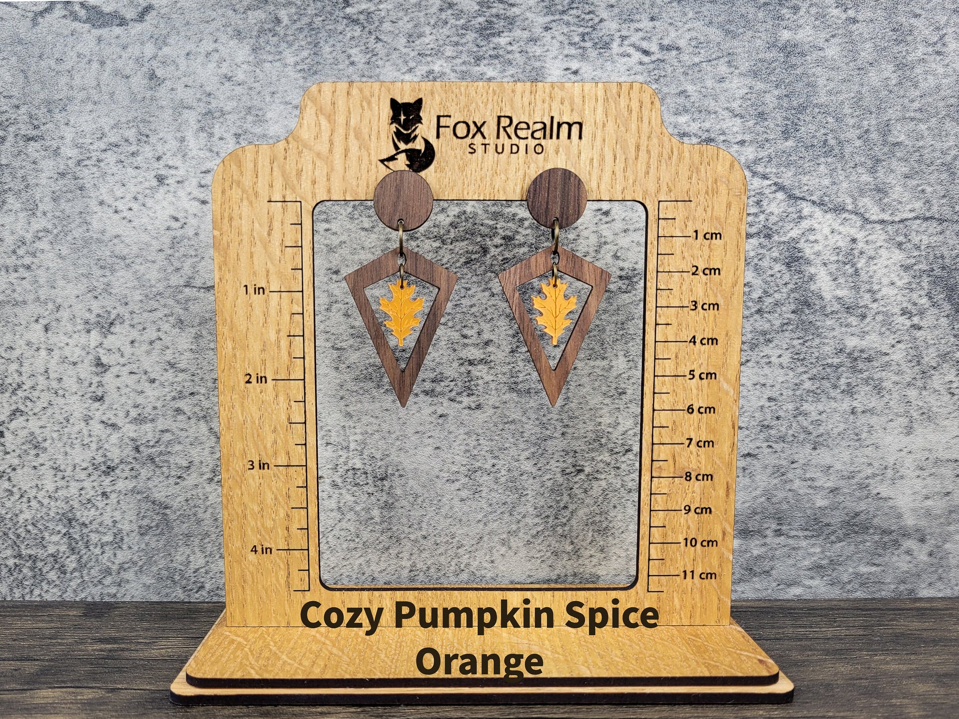 Wooden earring display card with 'Cozy Pumpkin Spice Orange' earrings on a textured gray background.