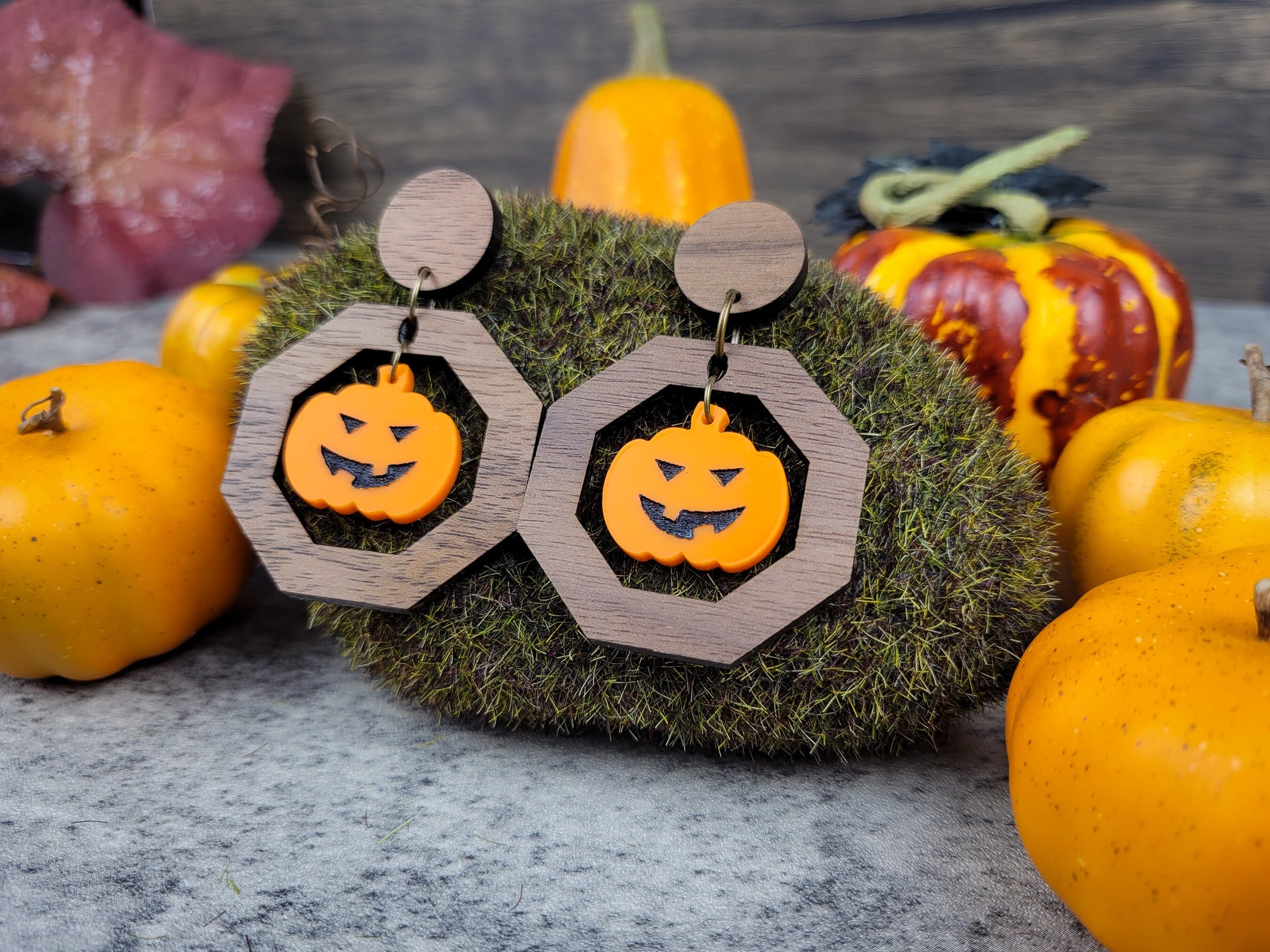 Halloween-themed earrings with pumpkin design on a decorative stand with pumpkins in the background.