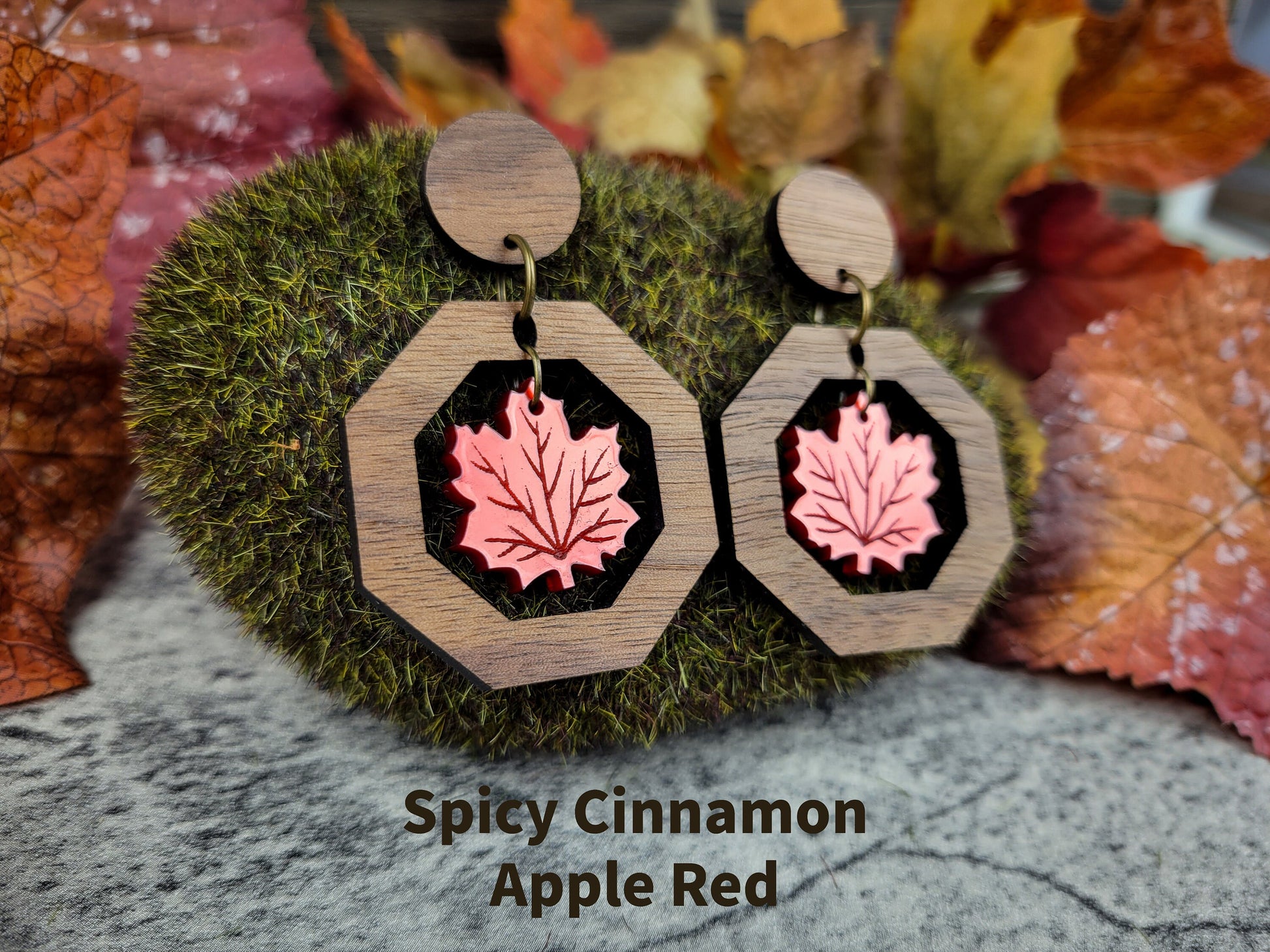 Wooden earrings with pink leaf design on a moss and leaf background, labeled 'Spicy Cinnamon Apple Red'.