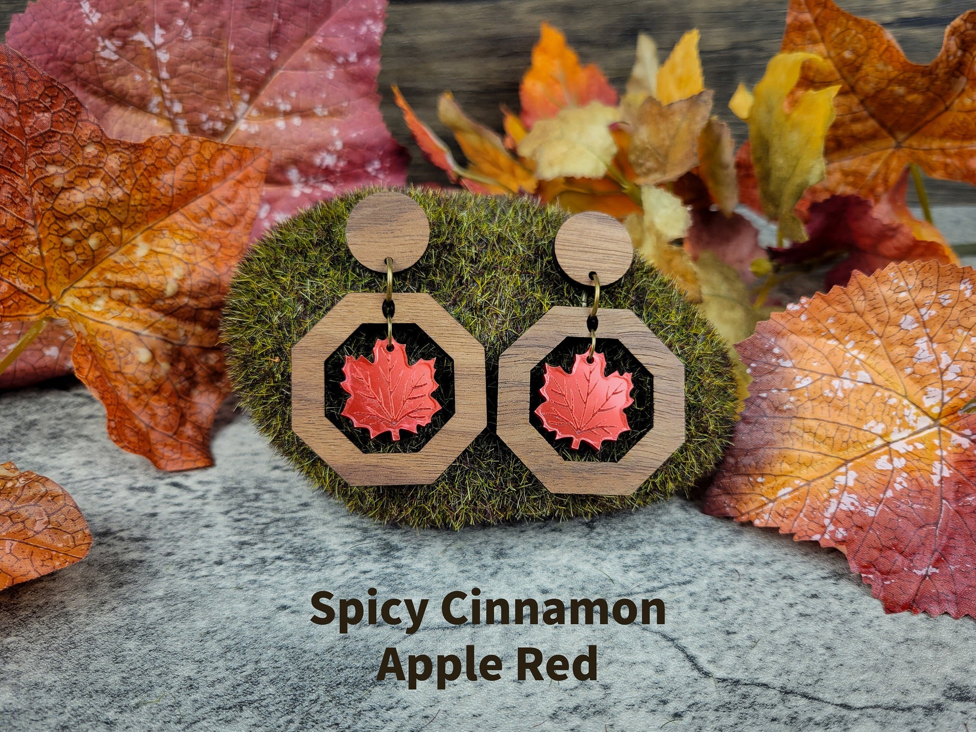Wooden earrings with red leaf design on a textured surface with autumn leaves.