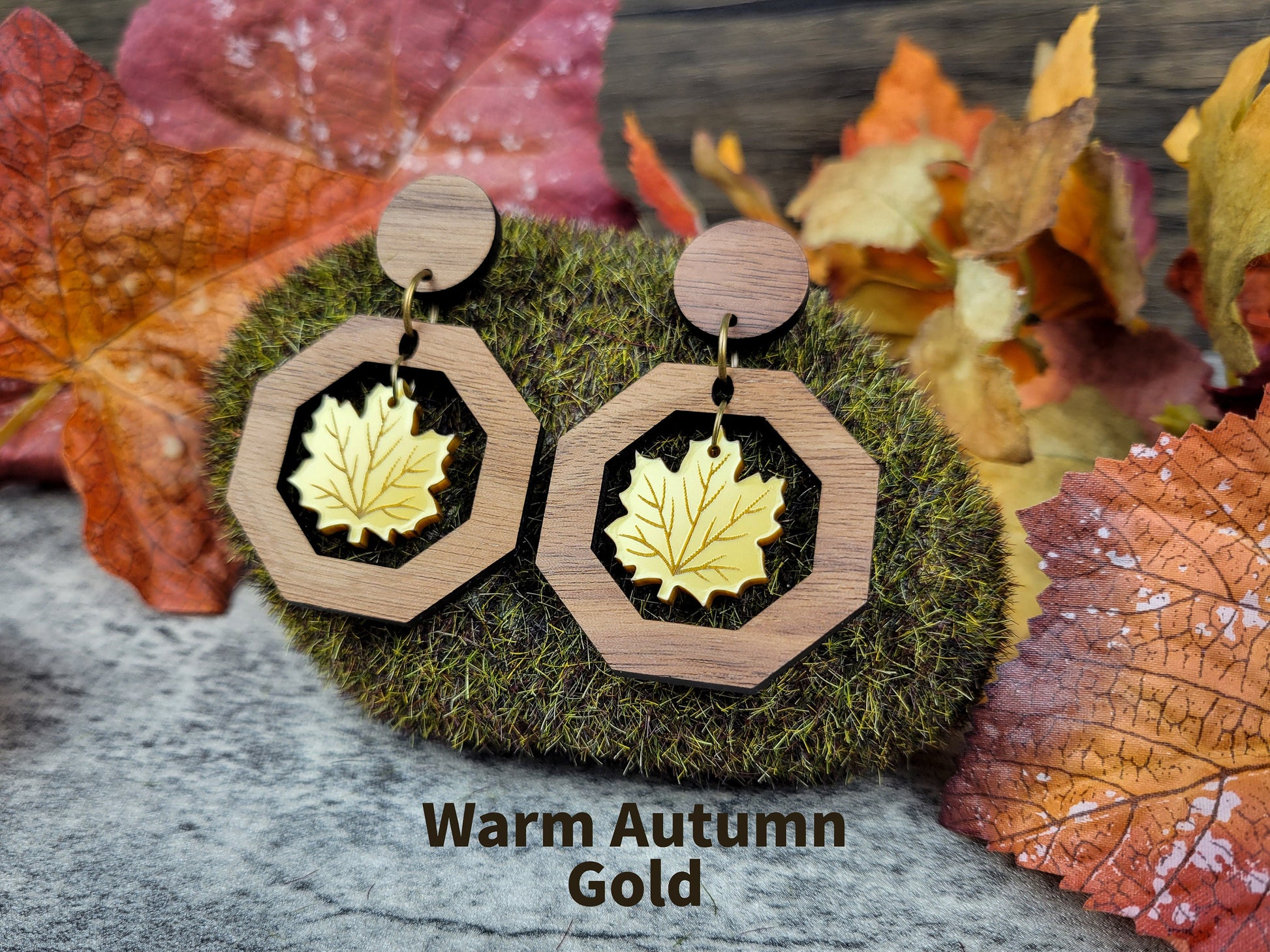 Wooden earrings with gold leaf design on a background of autumn leaves.