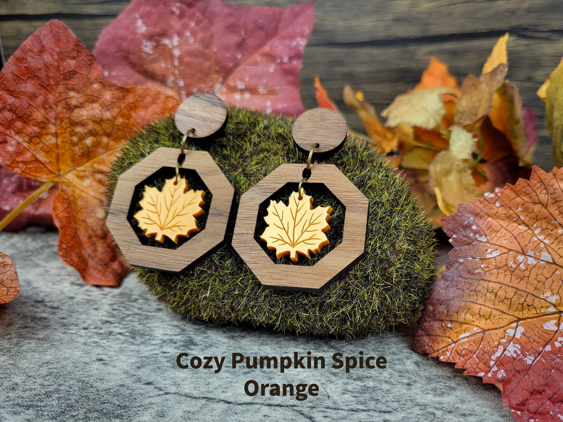 Wooden earrings with leaf design on a moss ball surrounded by autumn leaves.