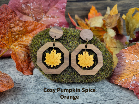 Wooden earrings with gold leaf design on a textured surface with autumn leaves.