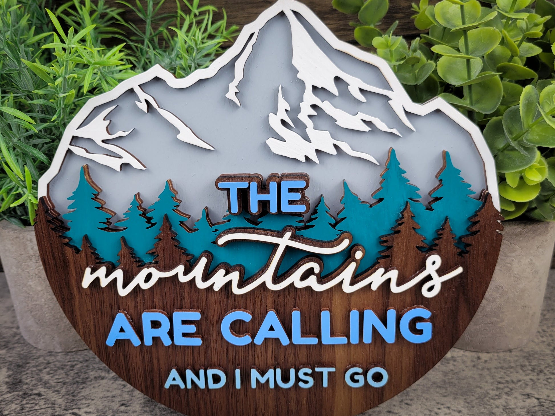 Decorative sign with mountain design and text 'The mountains are calling and I must go' on a wooden base.