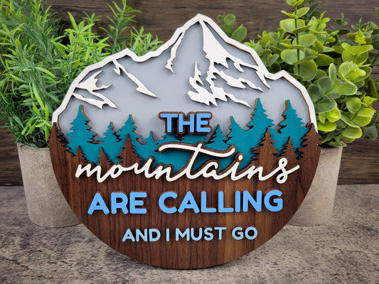 Decorative sign with mountain design and text 'The mountains are calling and I must go' surrounded by plants.