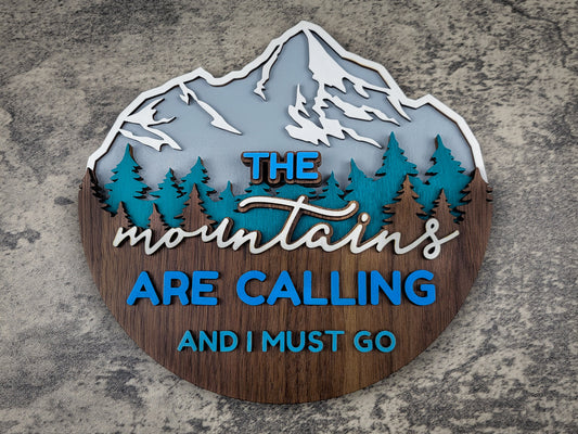 Decorative sign with mountain design and text 'The mountains are calling and I must go' on a textured surface.