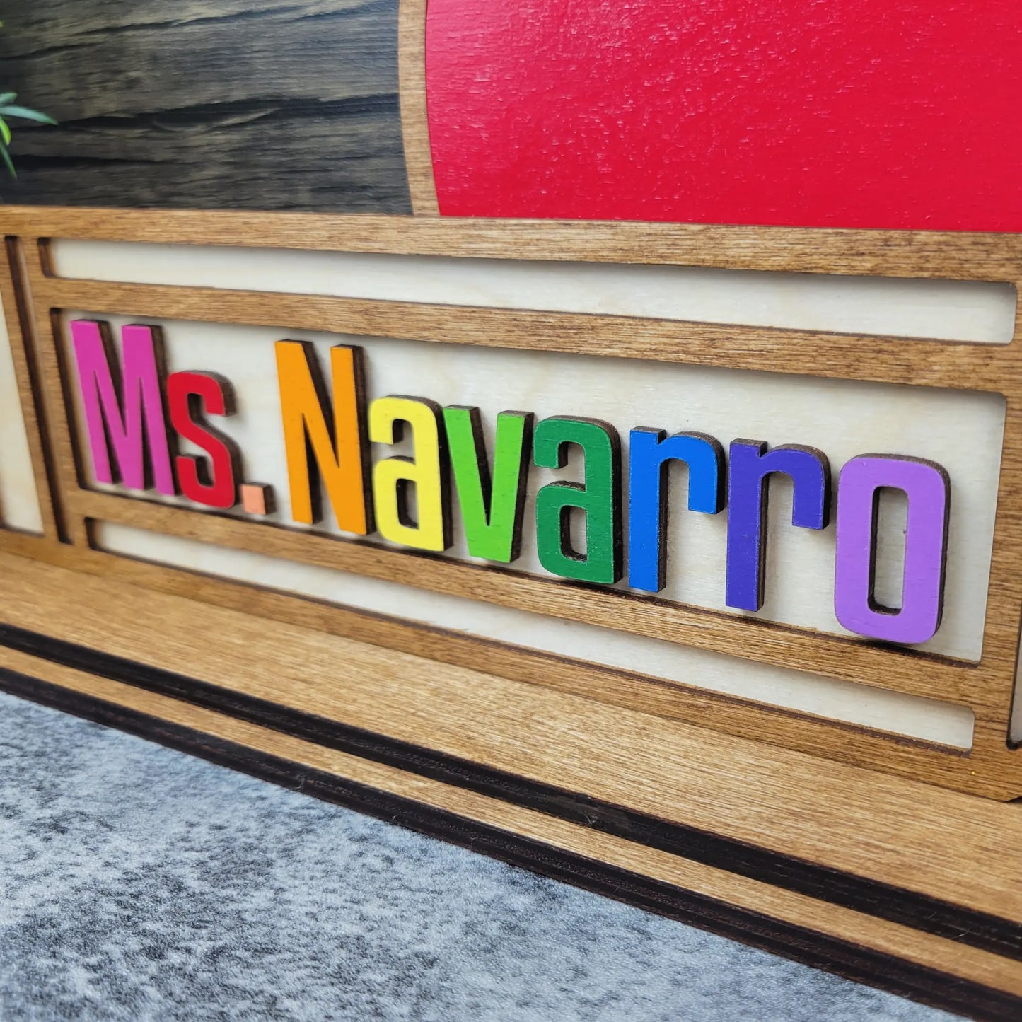 Colorful nameplate with 'Ms. Navarro' on a wooden frame against a red and gray background