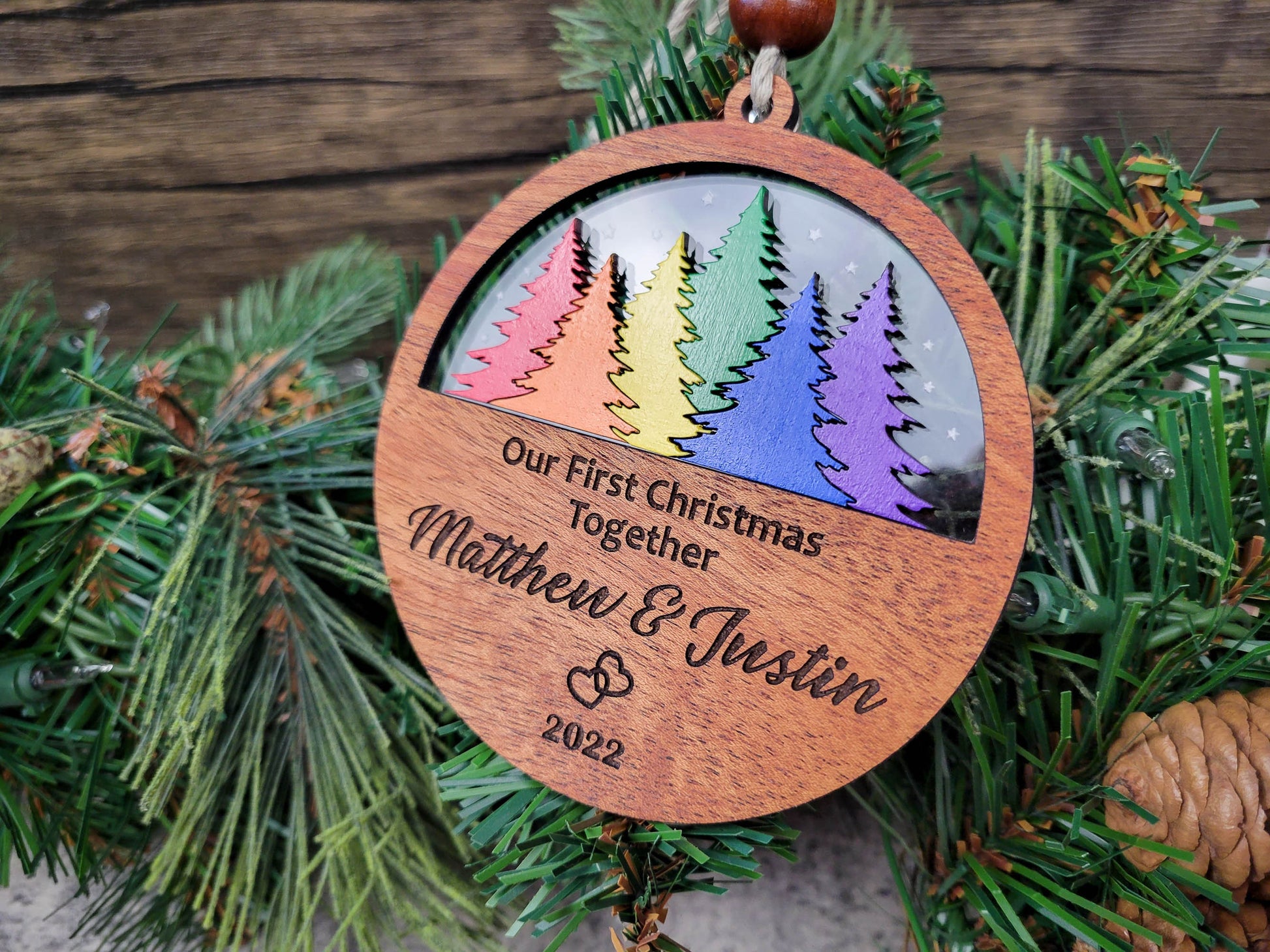 Wooden ornament with rainbow trees and engraved text on a Christmas tree.