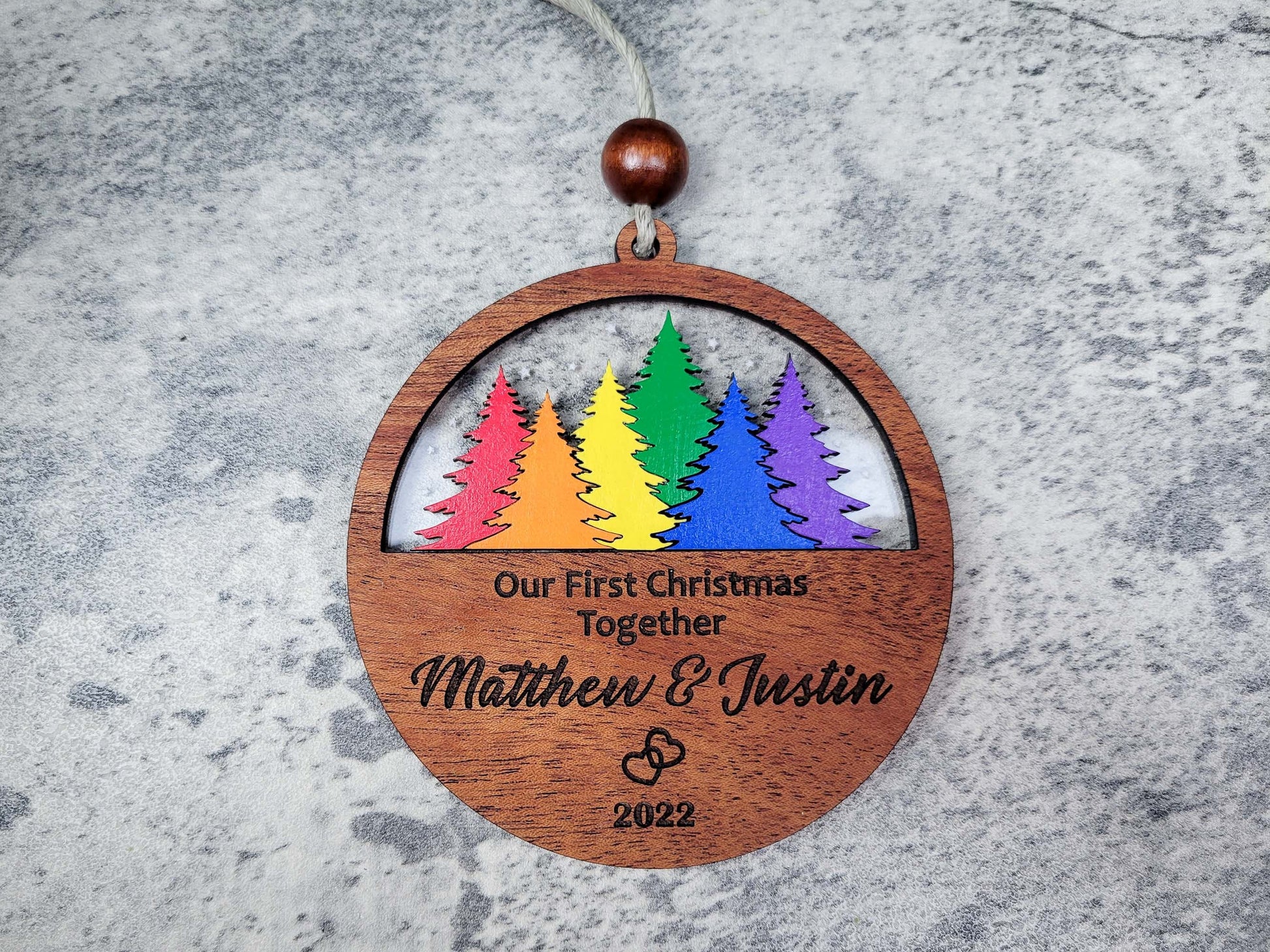 Wooden ornament with rainbow trees and engraved text on a gray surface