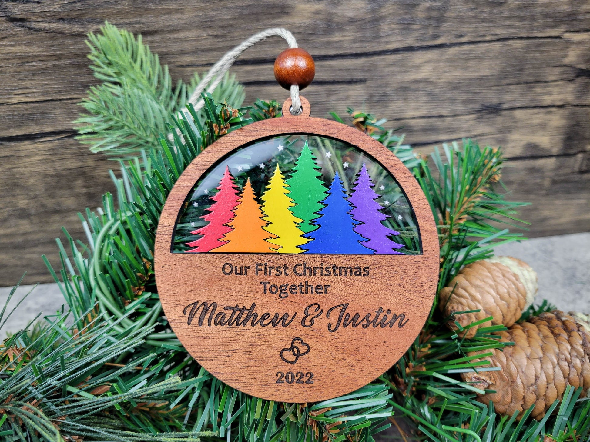 Wooden ornament with rainbow trees and engraved text on a Christmas tree branch.