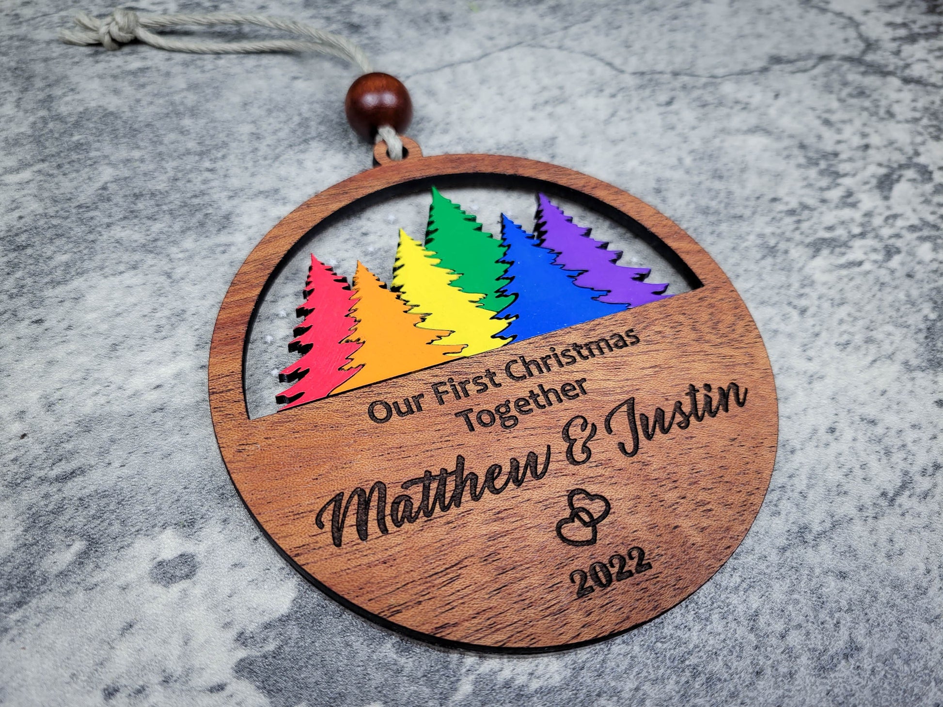 Wooden ornament with rainbow trees and engraved text on a gray surface