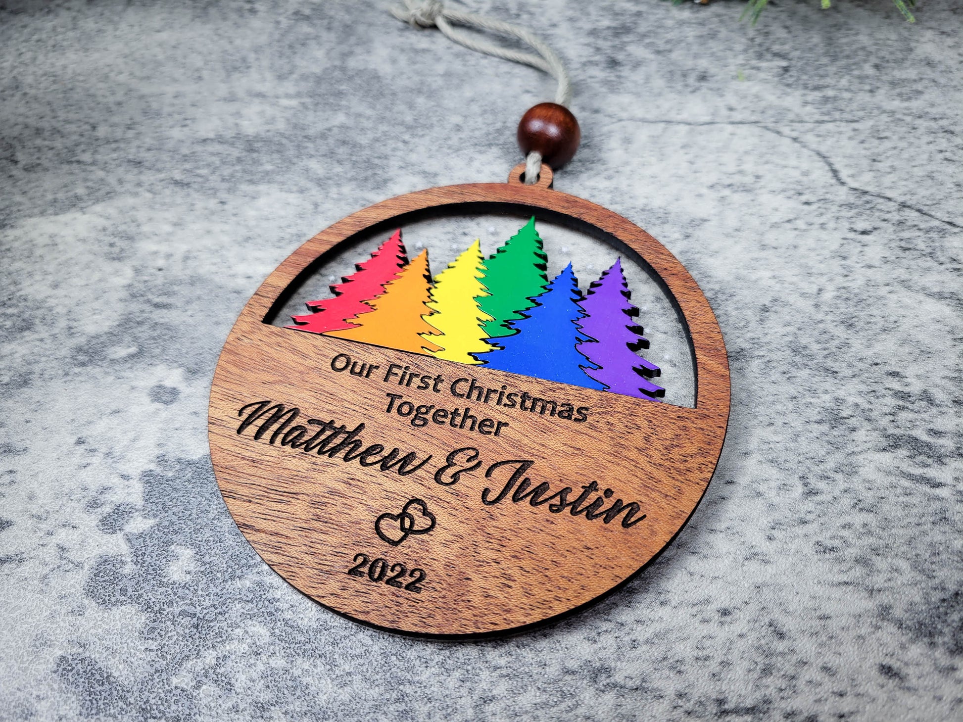 Wooden ornament with rainbow trees and engraved text on a gray surface