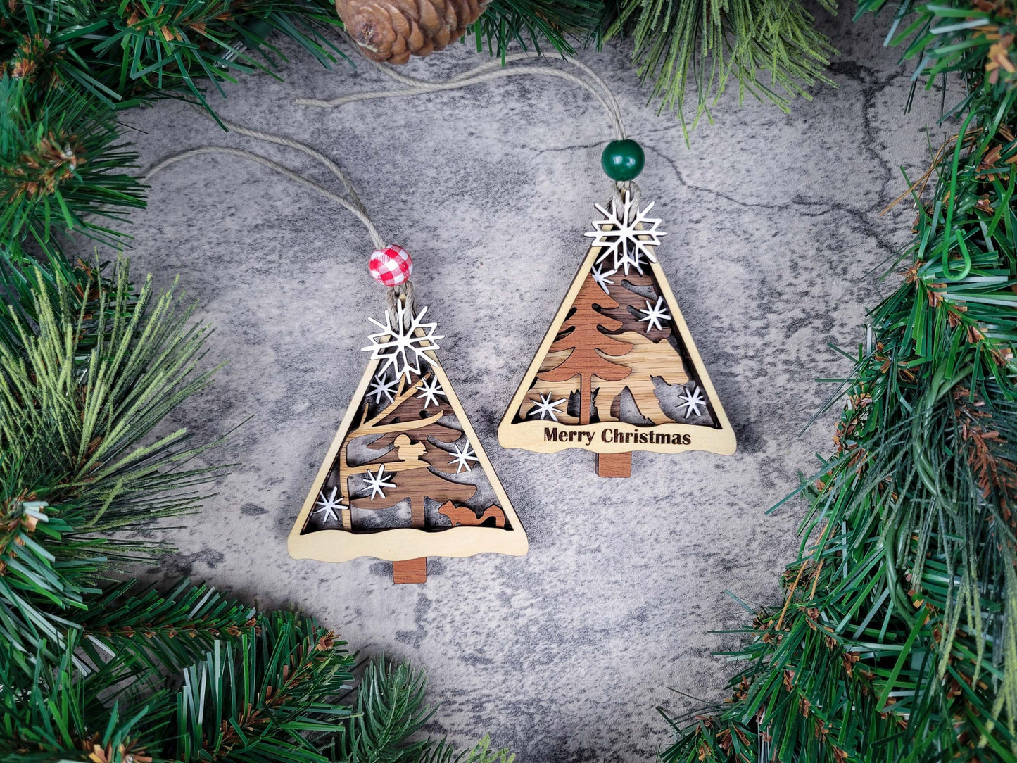 Wooden Christmas tree ornaments with festive designs on a textured surface surrounded by greenery.