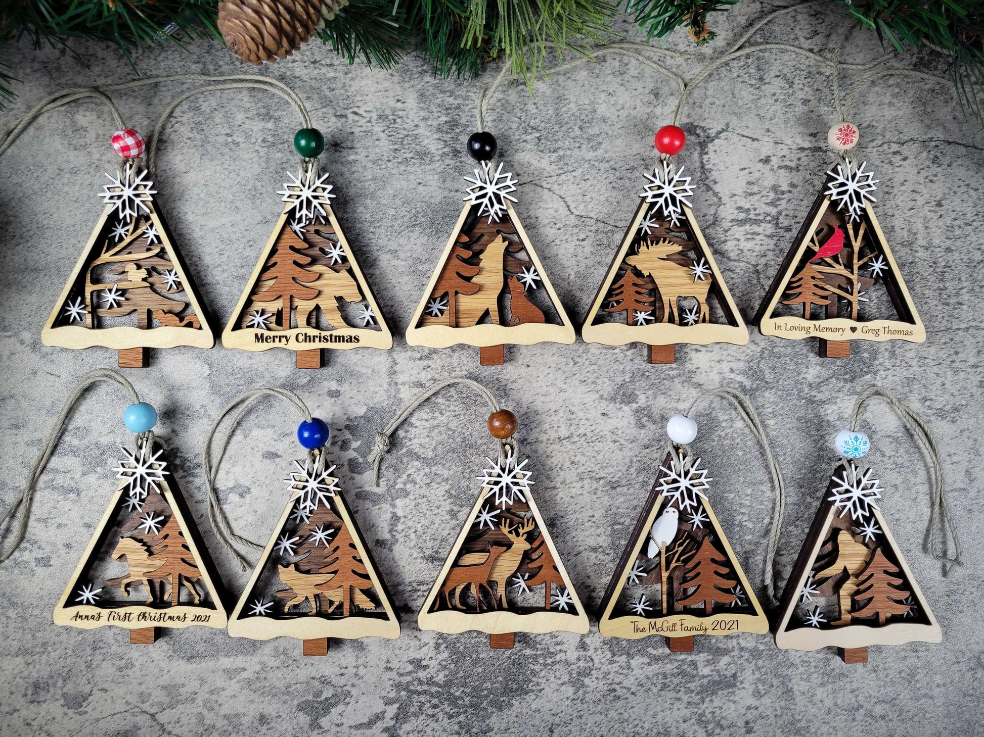 Set of triangular wooden Christmas tree ornaments with nature-themed designs on a textured surface.