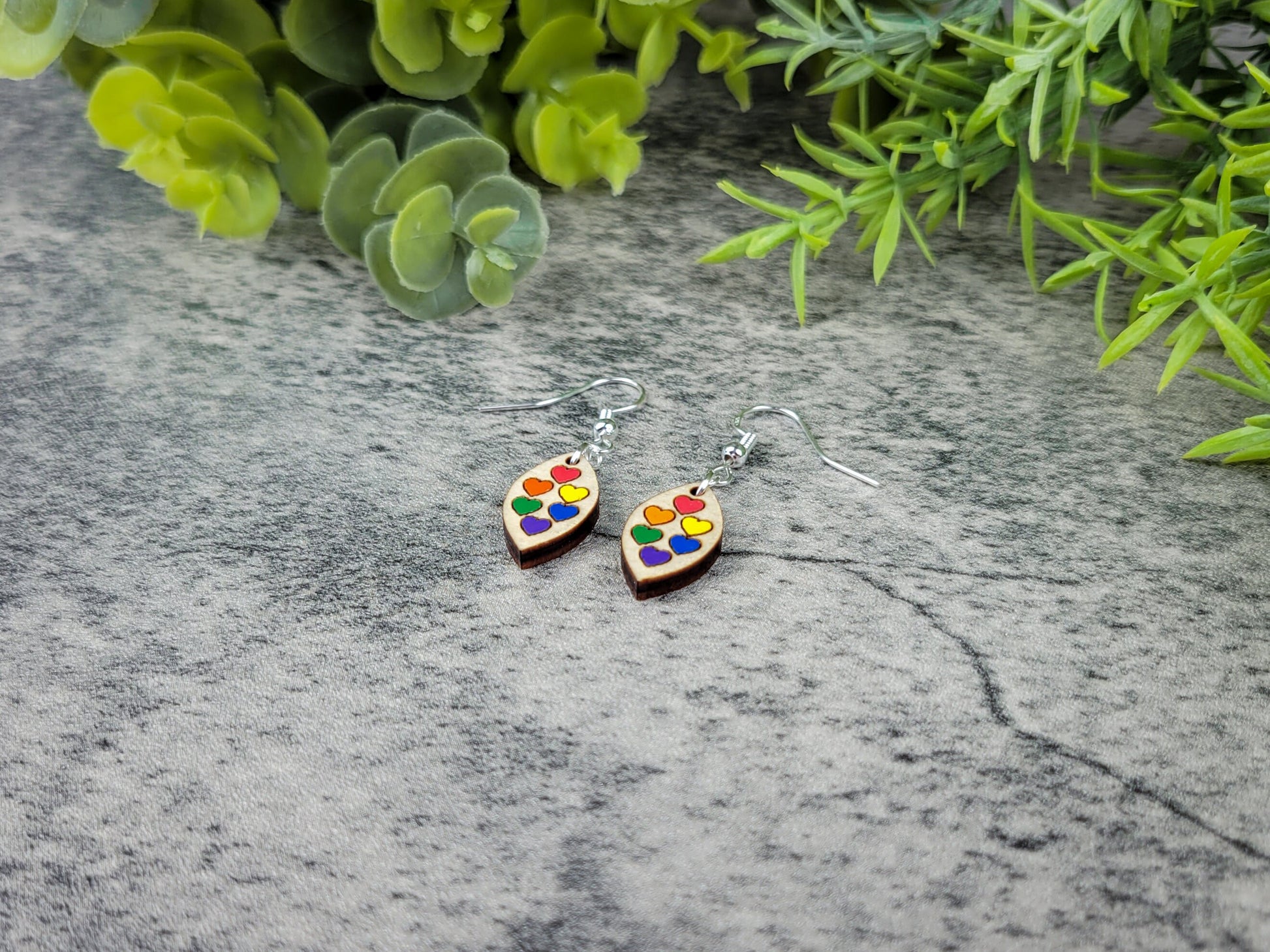 Heart-shaped earrings with colorful design on a gray surface with greenery