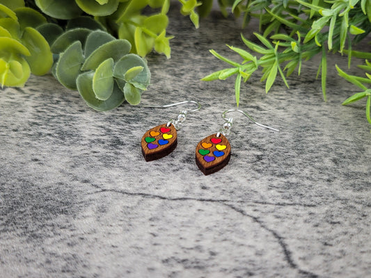 Wooden earrings with colorful heart design on a textured surface with greenery
