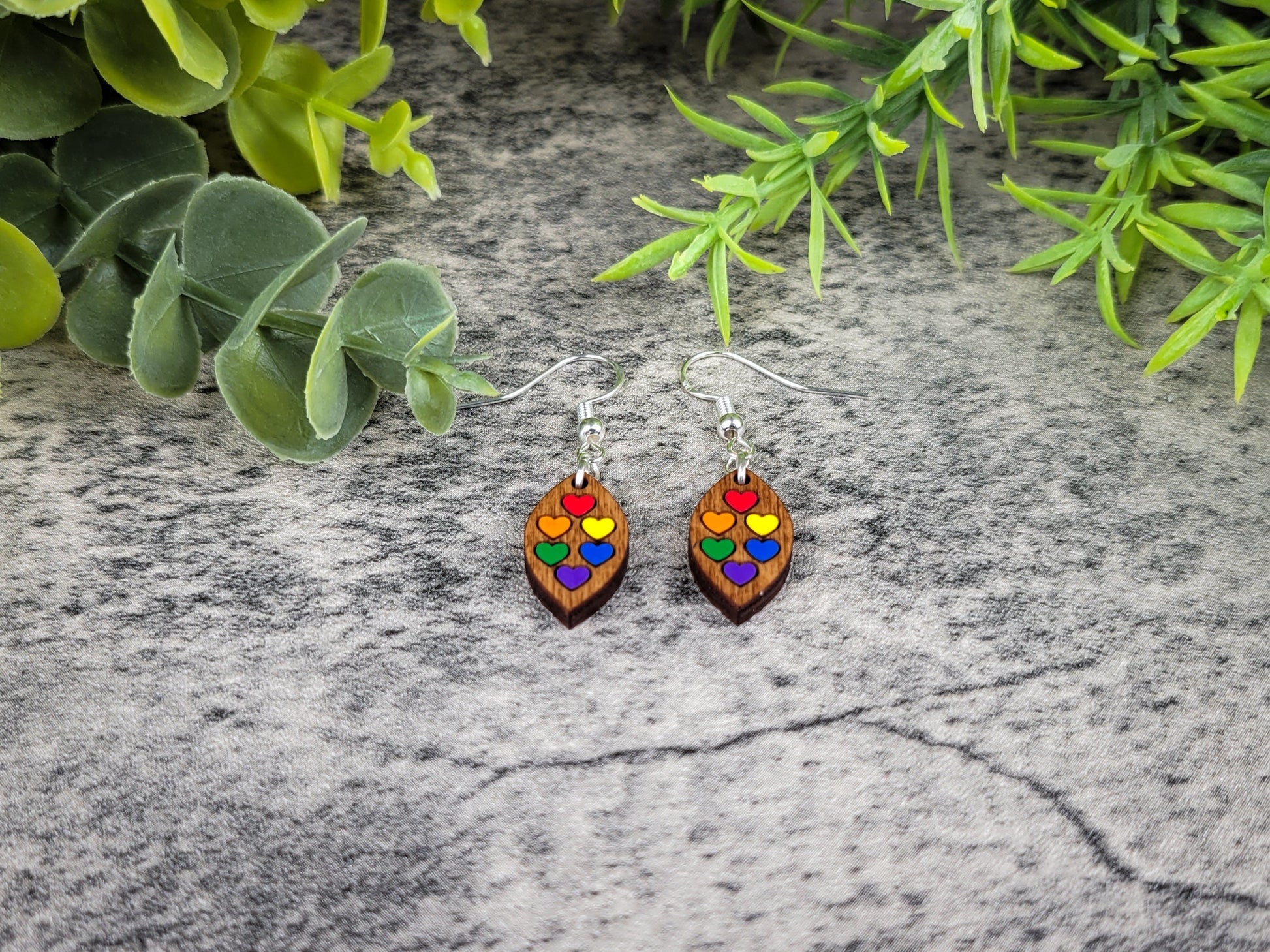Colorful heart-shaped earrings on a textured surface with green leaves in the background