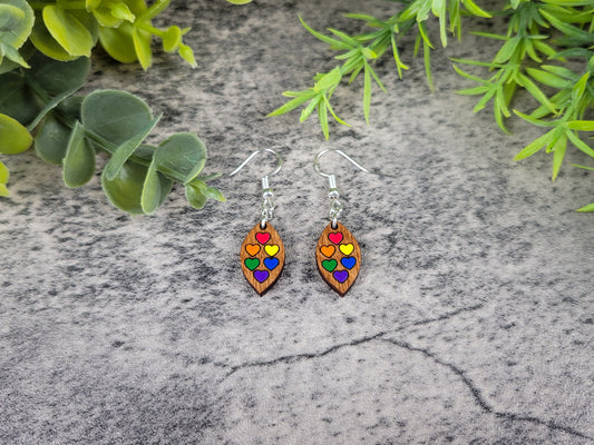Colorful heart-shaped earrings on a textured surface with green leaves.