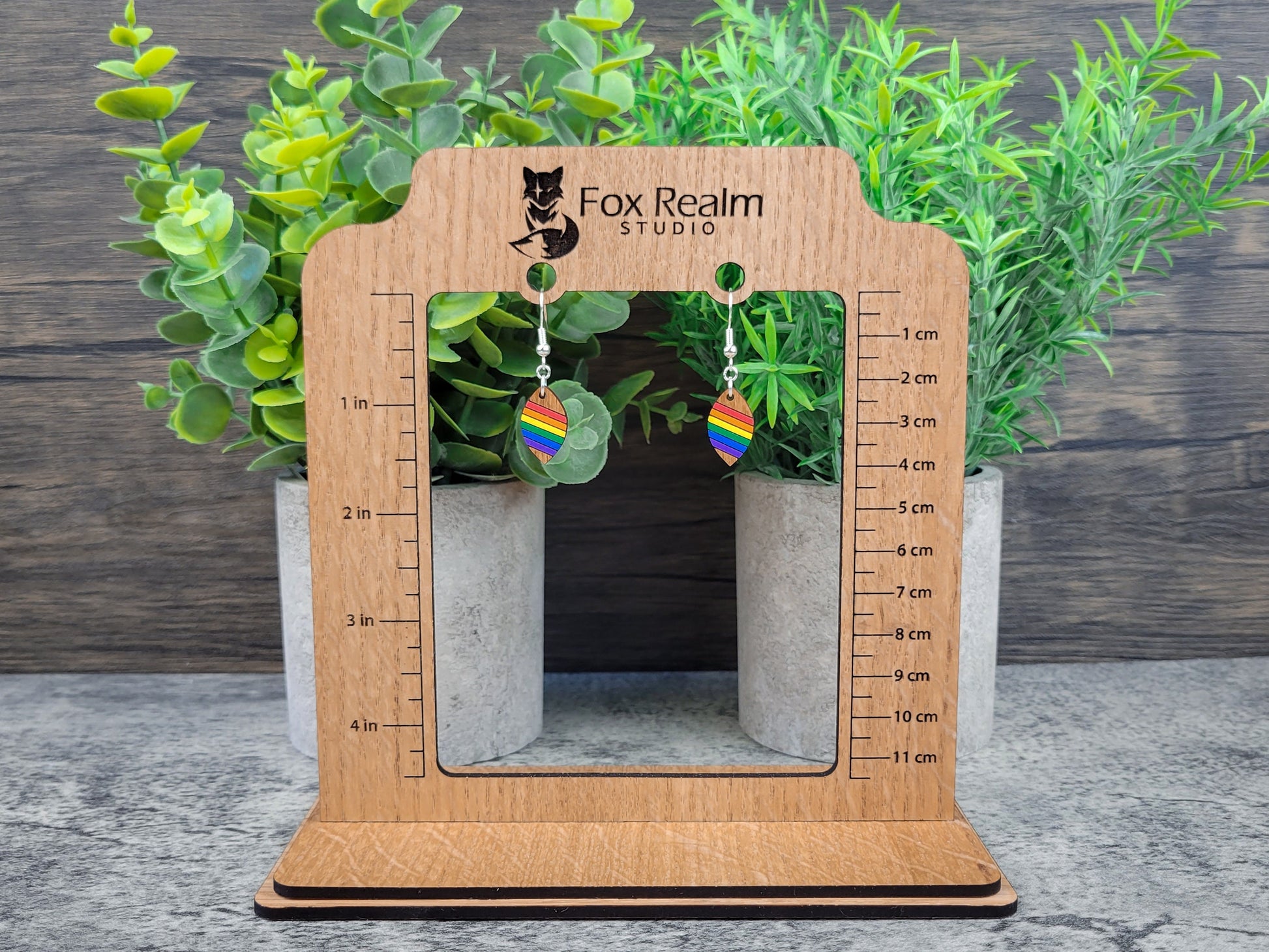 Wooden earring display with measurement scale, featuring rainbow earrings against a wooden background.