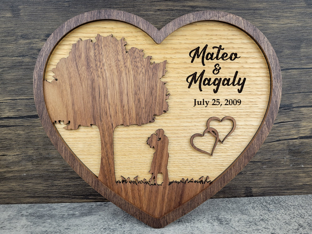 Wooden heart-shaped plaque with engraved tree, person, and heart, featuring names and date.