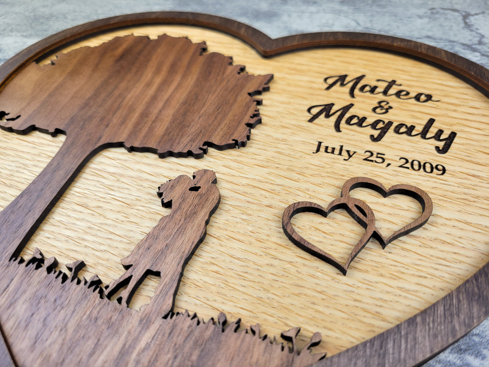 Wooden heart-shaped plaque with engraved couple's name and date, featuring cut-out silhouettes of a couple and two hearts.