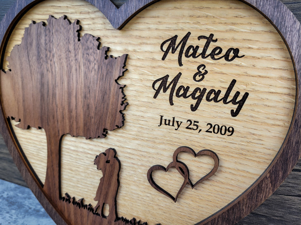 Wooden heart-shaped plaque with engraved tree, couple, and hearts, featuring names and date.