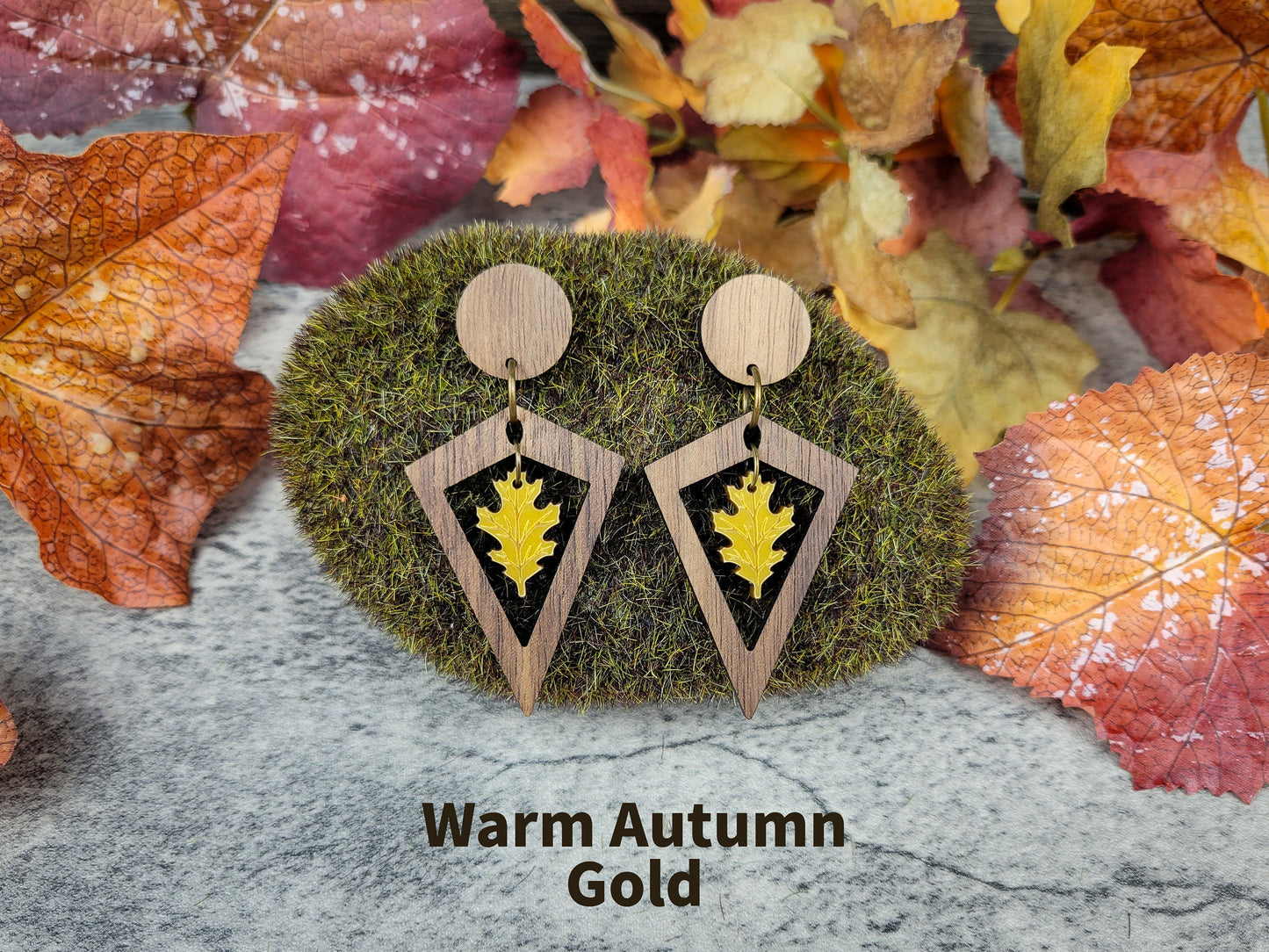 Wooden earrings with leaf design on a moss ball and autumn leaves background