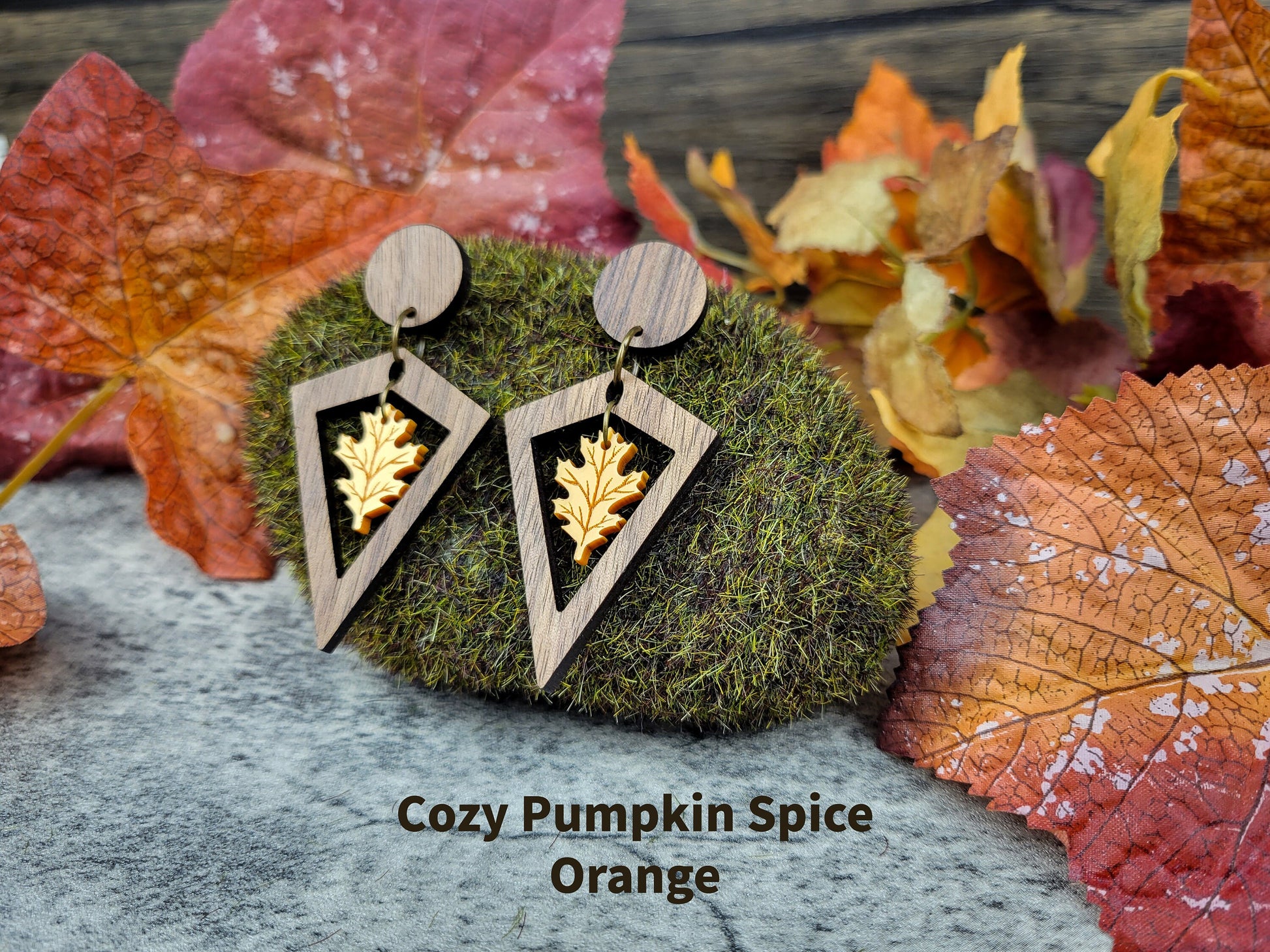 Wooden earrings with leaf design on a moss ball surrounded by autumn leaves.
