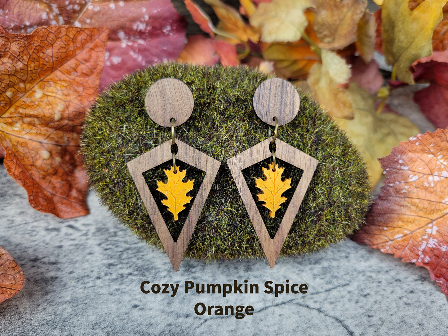 Wooden earrings with leaf design on a mossy background with autumn leaves.