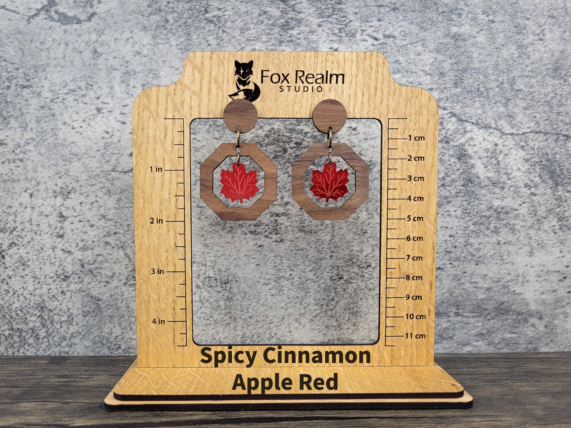Wooden earring display card with 'Spicy Cinnamon Apple Red' earrings on a textured surface.