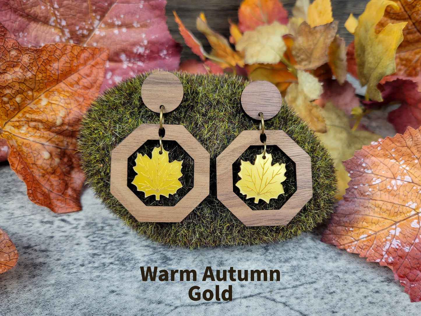 Wooden earrings with leaf design on a mossy surface with autumn leaves in the background